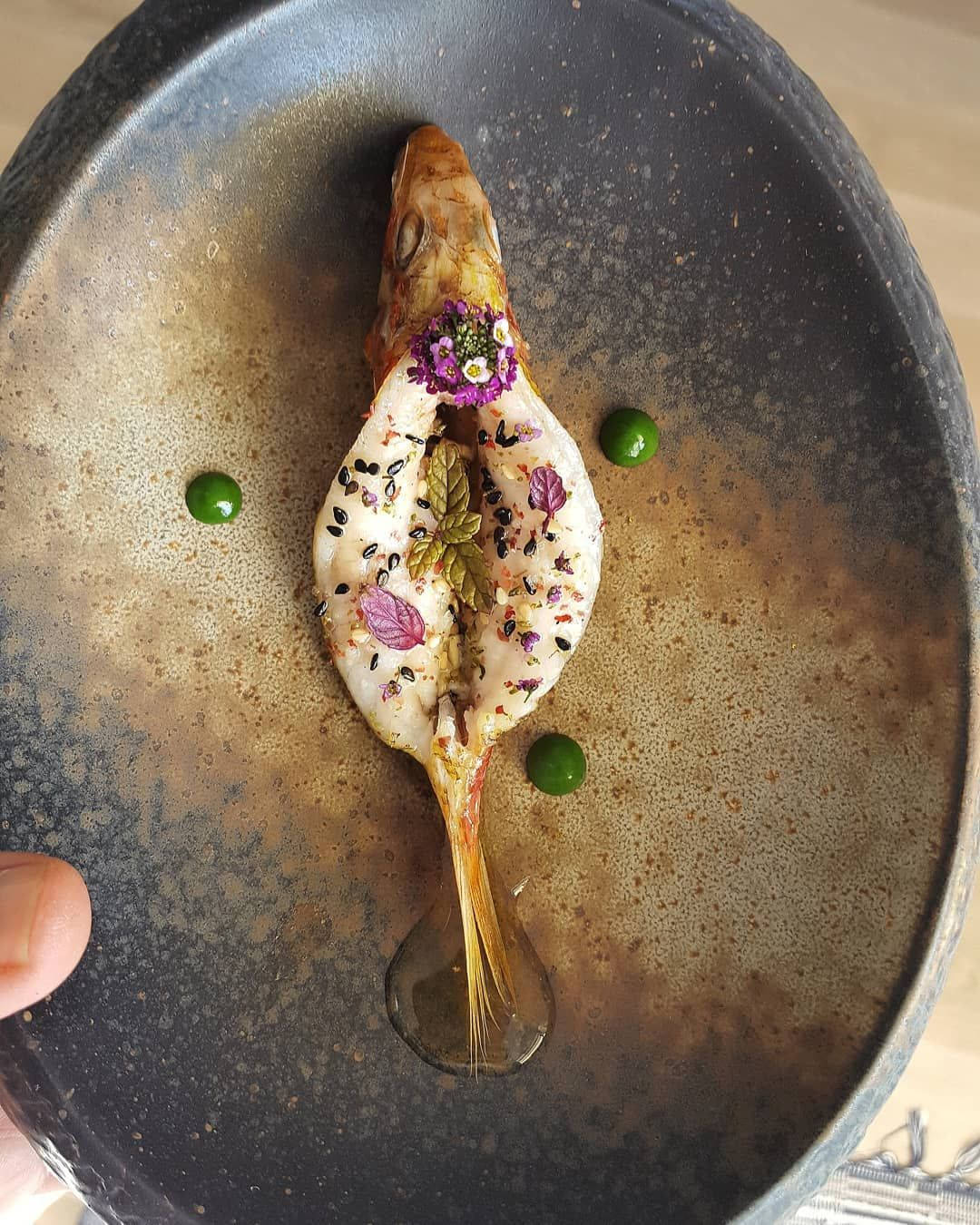 Delicious Food 桌布 壁紙 — 一整條烤魚優雅地擺放在一個質樸的陶瓷盤上，盤子飾以可食用花朵和綠色球體。