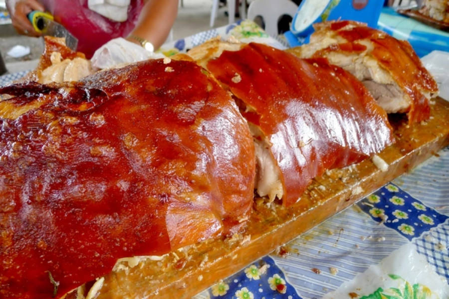 Pig 桌布 壁紙 — 一整隻烤豬，表皮焦糖化酥脆，切片放在木盤上，置於有圖案的桌布上。