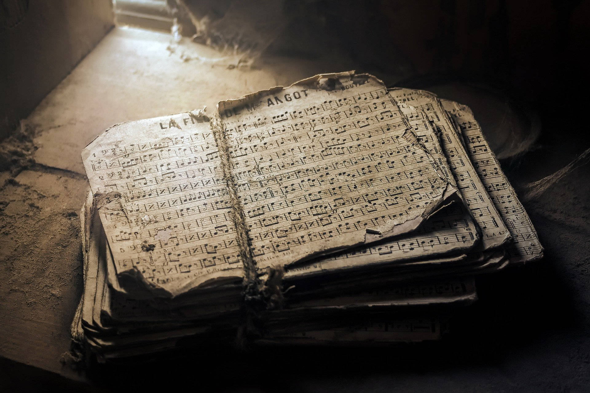 old 桌布 壁紙 — 一本古老風化的樂譜書在窗邊柔和的自然光下打開，放在佈滿灰塵的地板上。