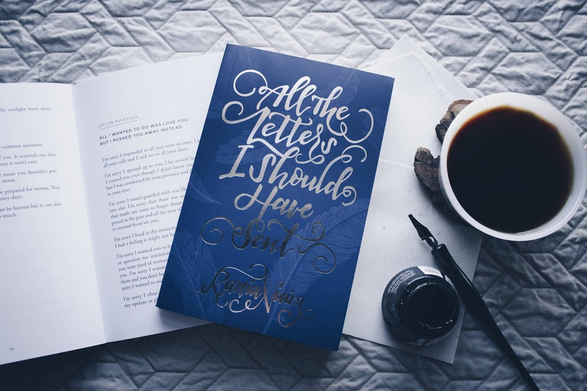藍色美學 桌布 壁紙 — 一本名為《All the Letters I Should Have Sent》的藍色書本打開著，旁邊放著一杯咖啡和一支鋼筆，置於絎縫灰色表面上。