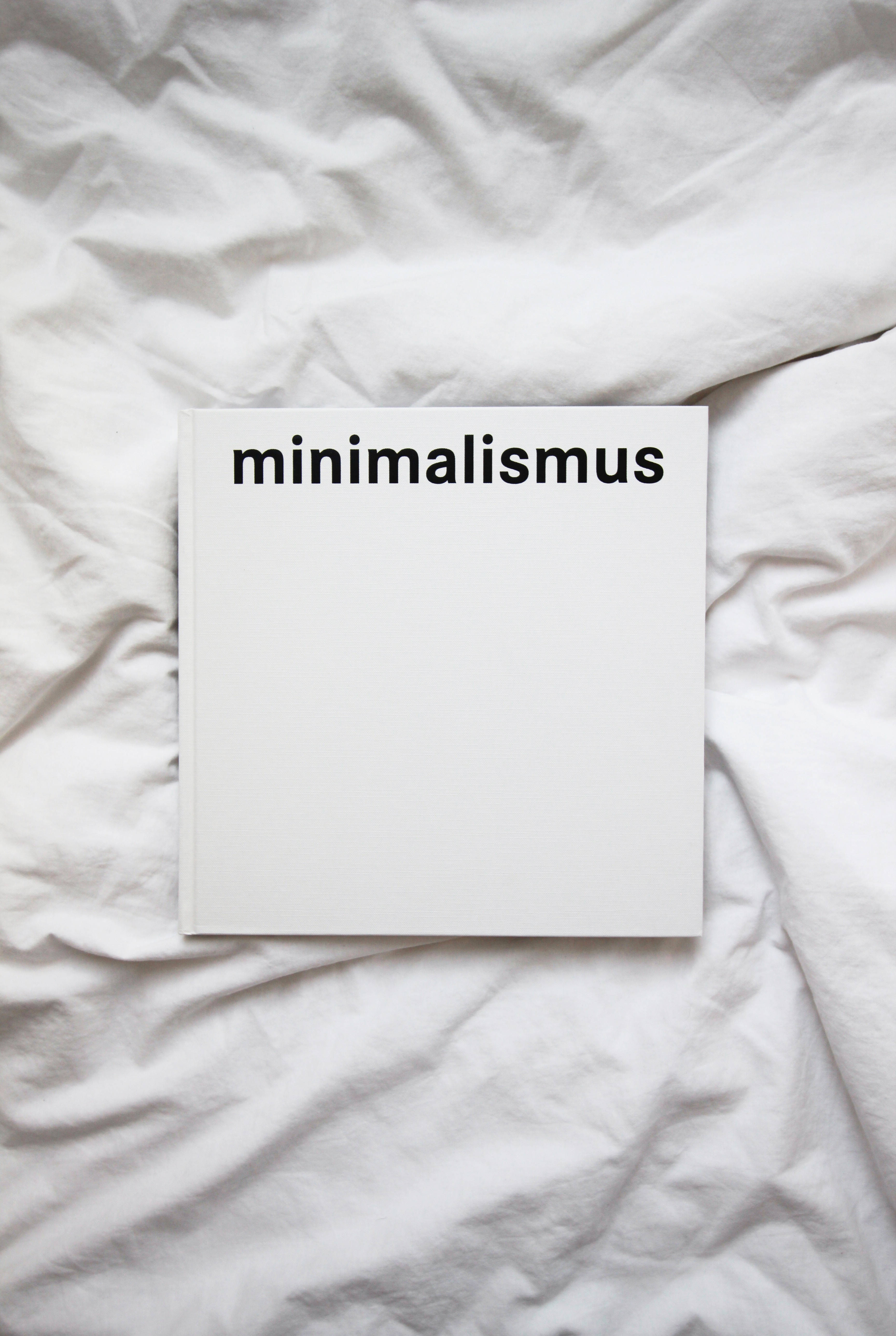 白色 桌布 壁紙 — 一本名為 minimalismus 的純白色書本，放在皺巴巴的白色床單上，構成極簡主義的構圖。