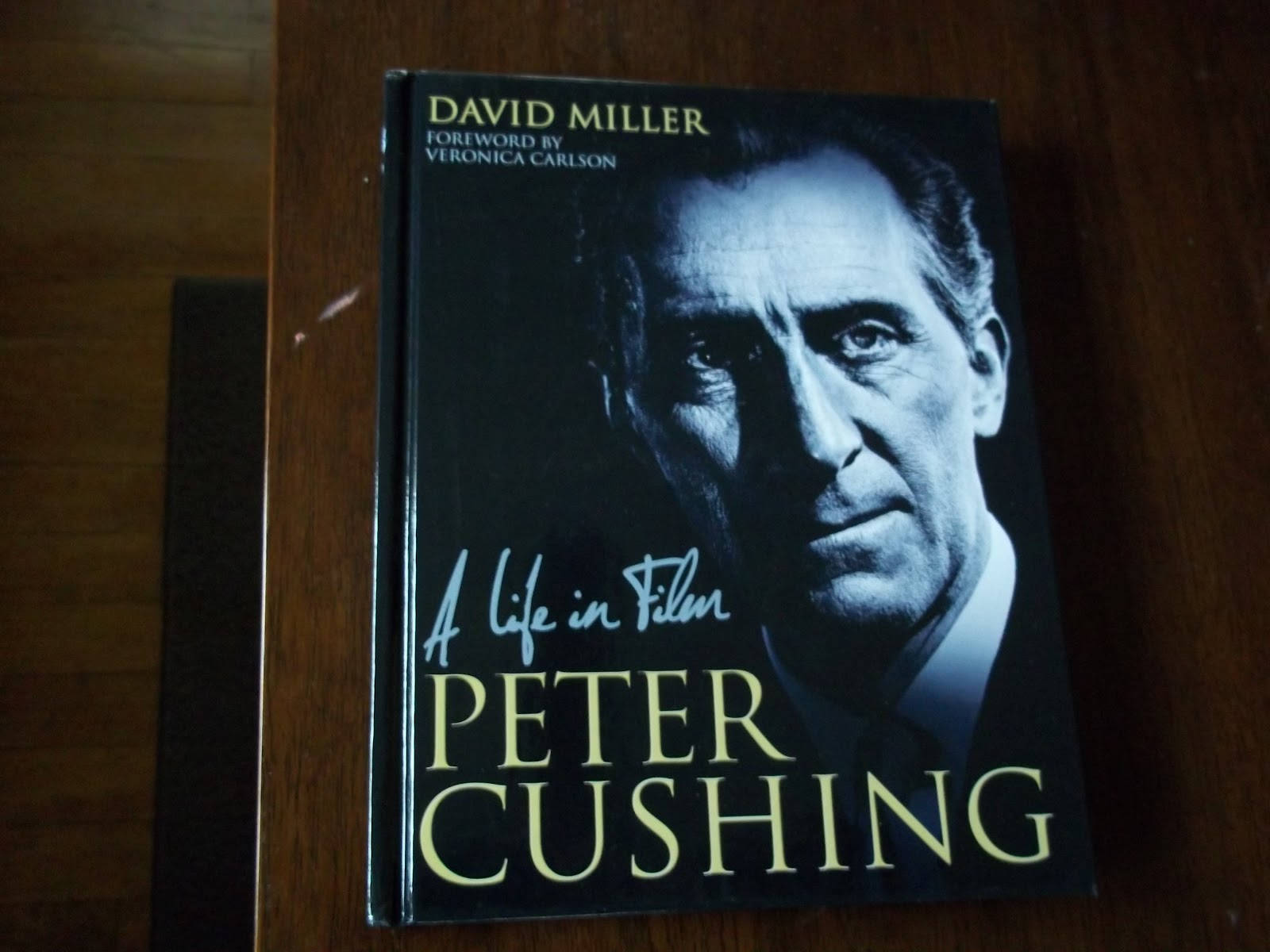 書本 桌布 壁紙 — 一本名為《Peter Cushing: A Life in Film》的簽名精裝書，在溫暖的燈光下放置在木質表面上。