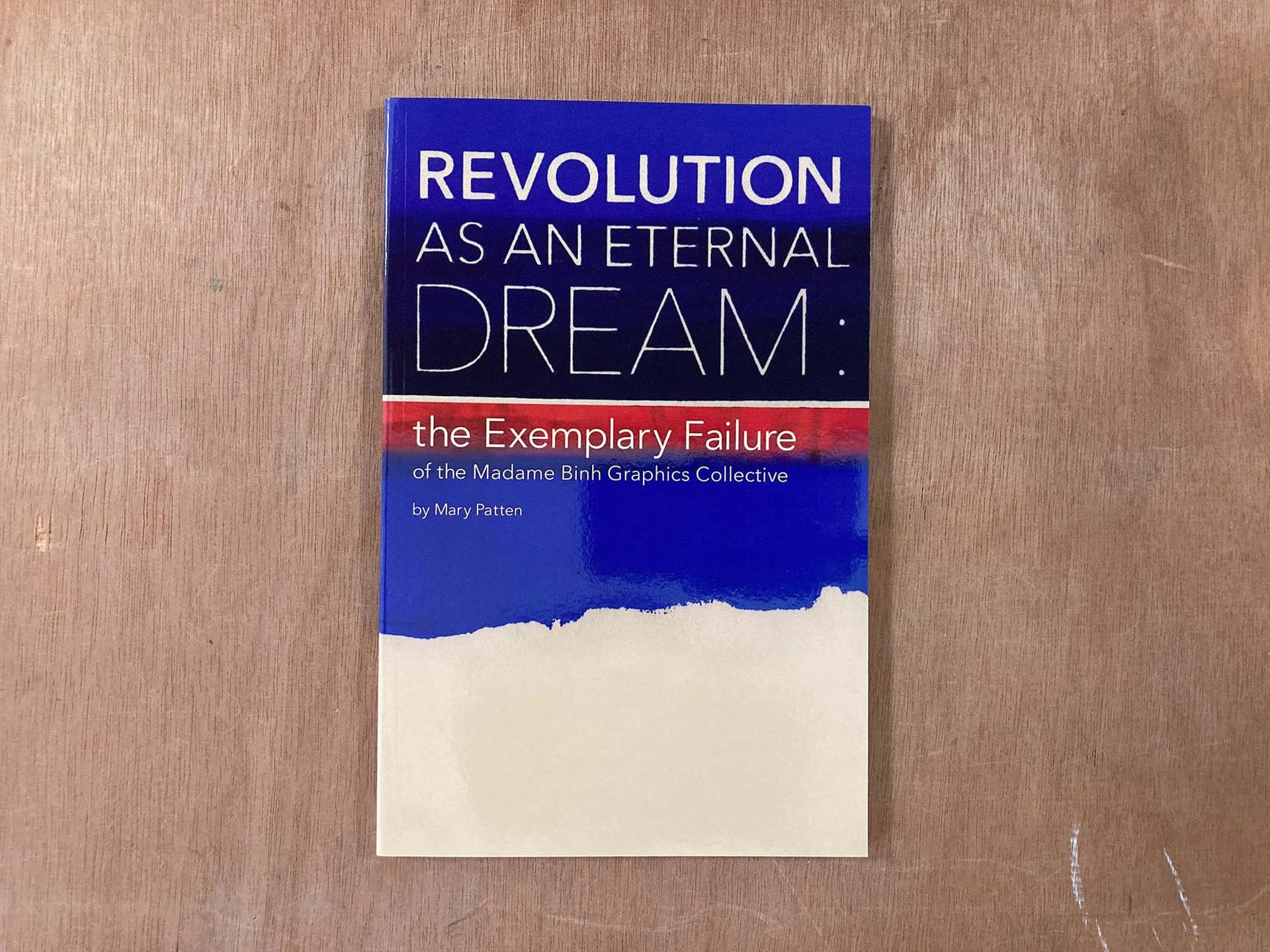 高清 桌布 壁紙 — 一本名為《Revolution as an Eternal Dream》的書放在淺棕色木質表面上，表面可見木紋和刮痕。