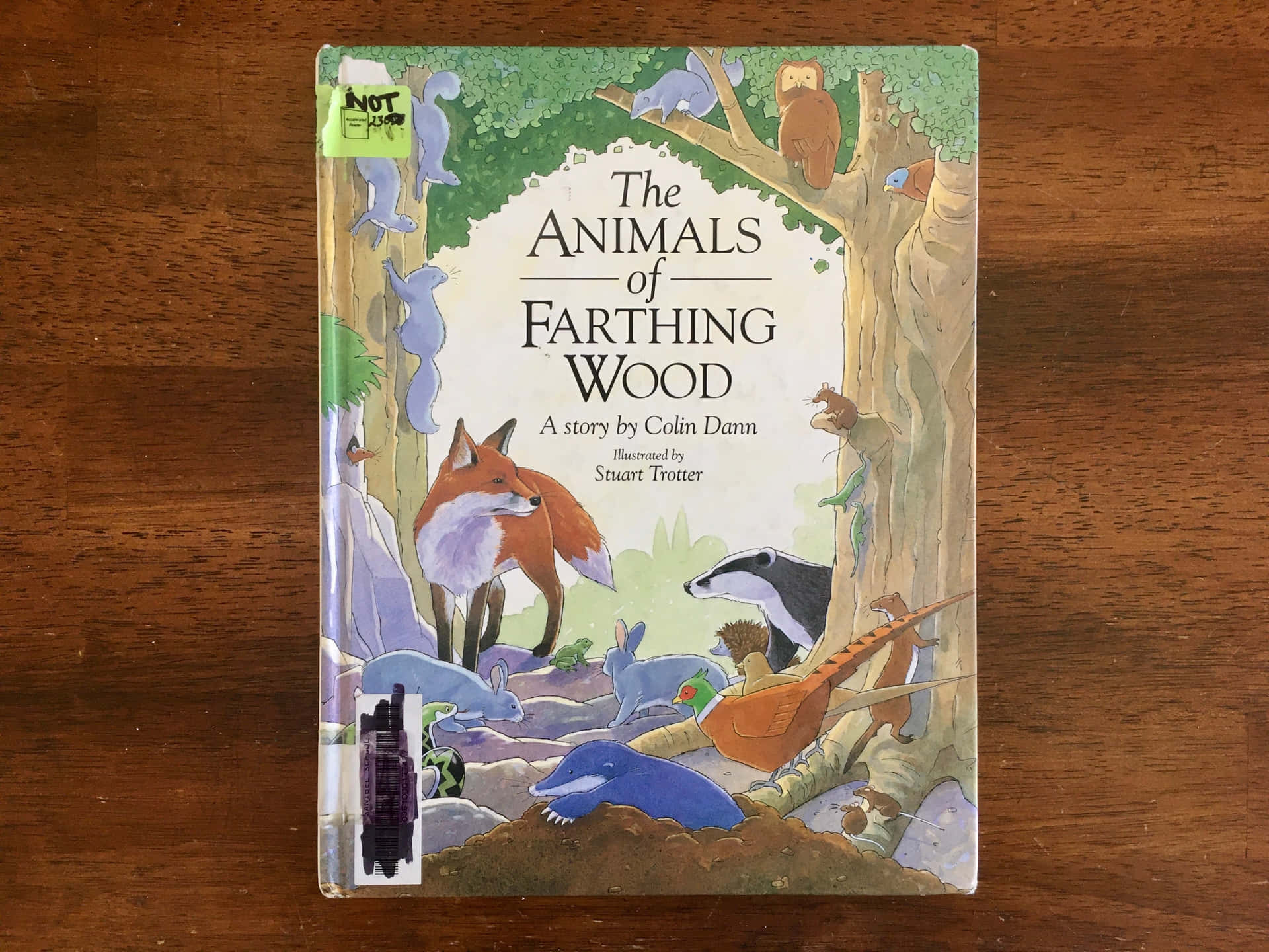 書本 桌布 壁紙 — 一本名為《The Animals of Farthing Wood》的兒童書放在木桌上，書脊上貼有綠色的「非賣品」貼紙。