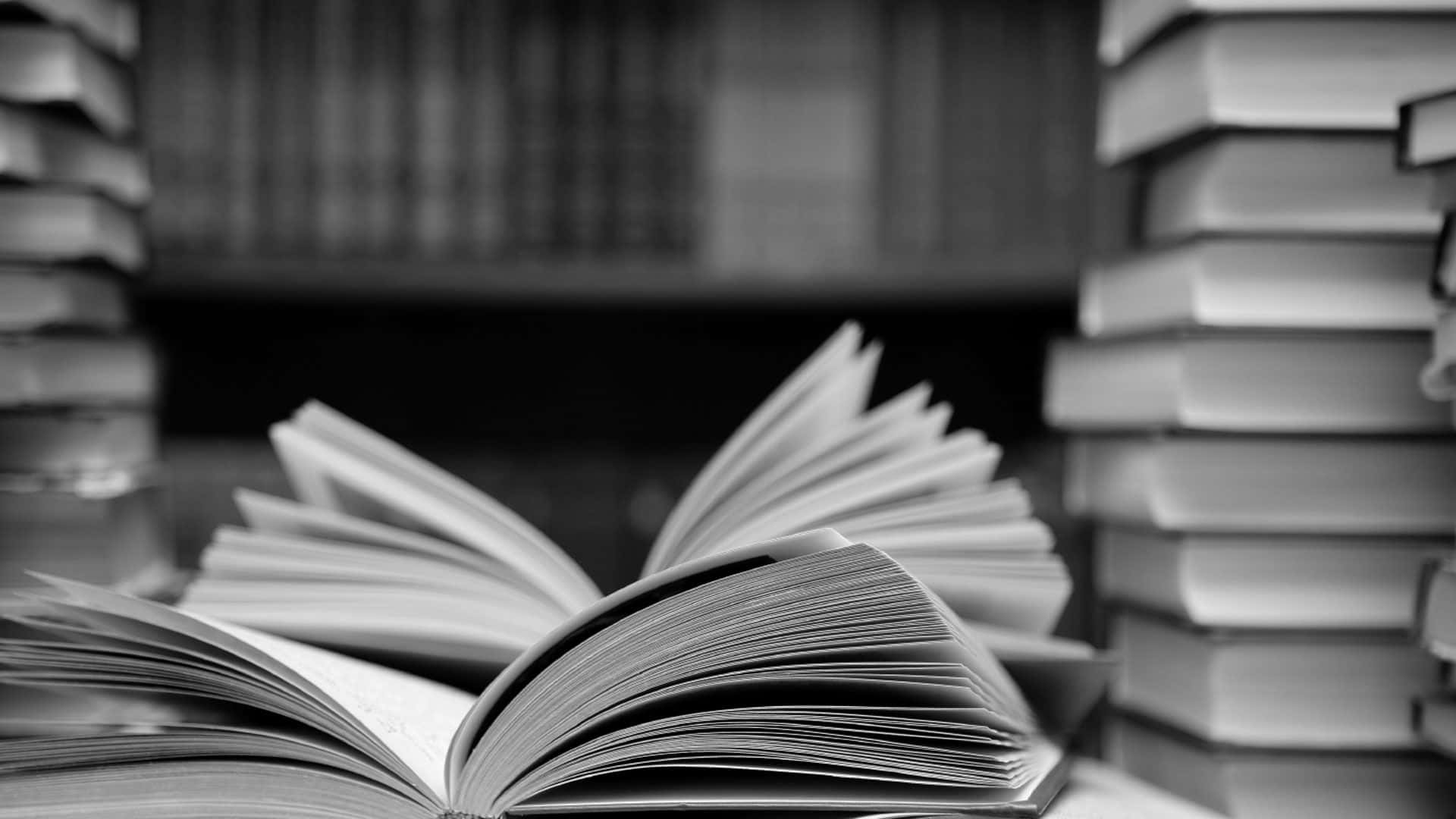 Black And White Book 桌布 壁紙 — 一本單色打開的書本放在寧靜圖書館書架上高聳的書堆之間。
