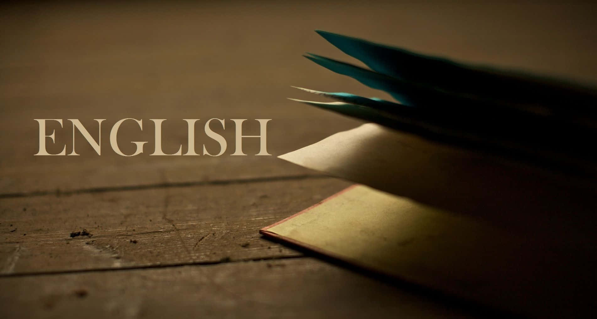 English 桌布 壁紙 — 一本復古書籍搭配青綠色羽毛筆，放在經風化的木桌上，優雅地展示著ENGLISH這個詞。