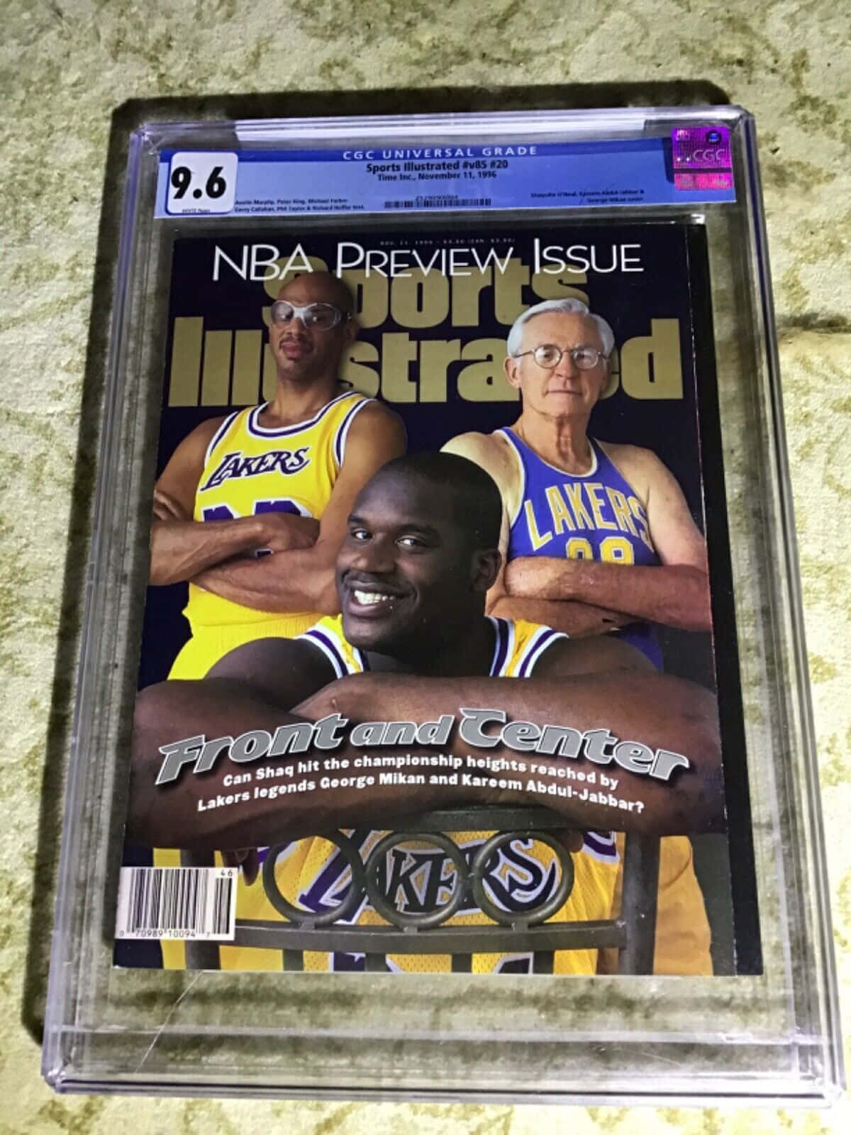 湖人 桌布 壁紙 — 一本復古的《體育畫報》雜誌，封面是Shaquille O'Neal、George Mikan和Kareem Abdul-Jabbar身穿湖人隊球衣，經CGC評級為9.6，放在有紋理的表面上。