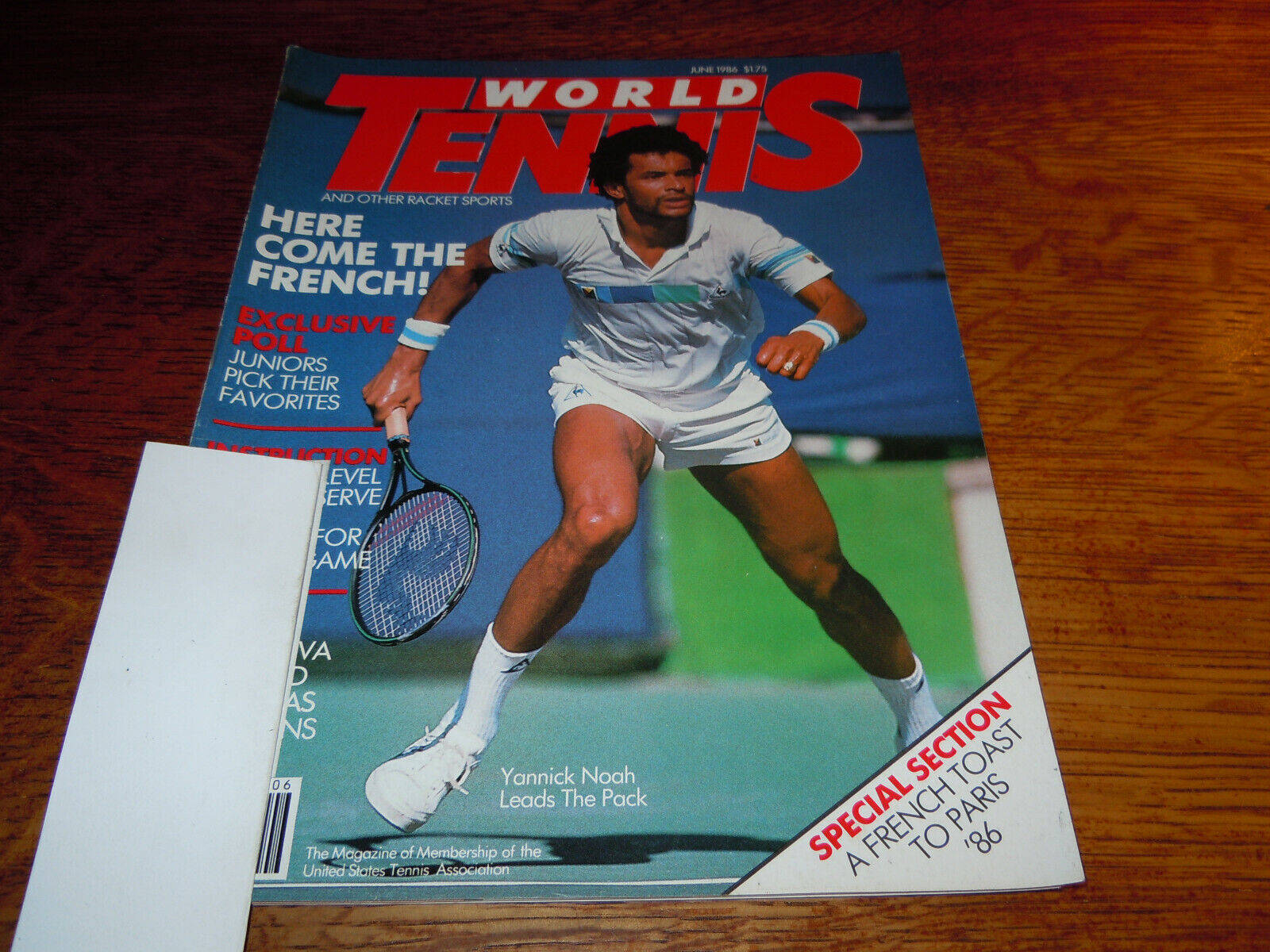Tennis 桌布 壁紙 — 一本復古的World Tennis雜誌封面， featuring Yannick Noah 在球場上揮拍中，放在木桌上。