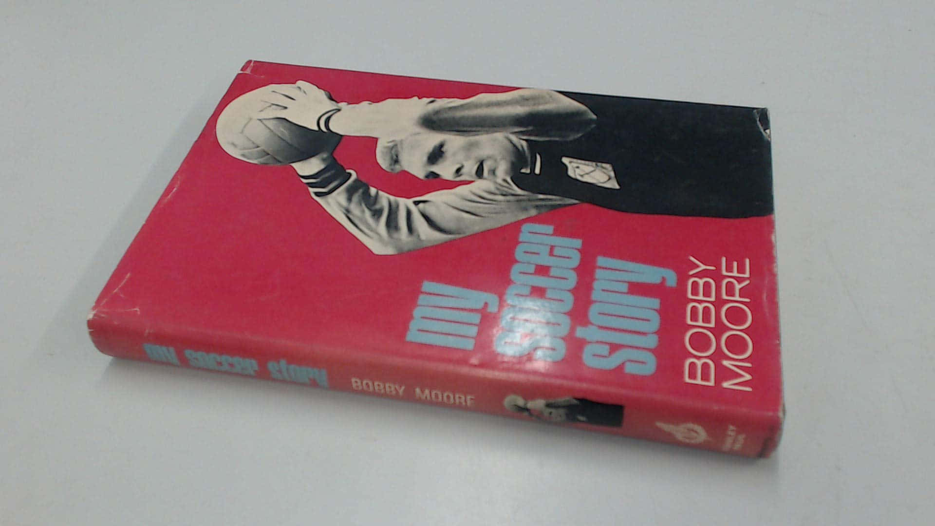 書本 桌布 壁紙 — 一本復古紅色書，名為《My Soccer Story》，作者Bobby Moore，封面有黑白照片，顯示一名足球員手持足球。