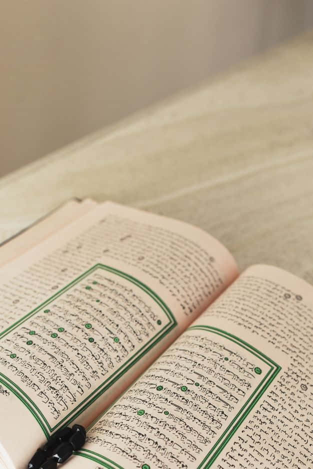 Quran 桌布 壁紙 — 一本打開的古蘭經，頁面帶有綠色邊框，放在柔軟的米色表面上，周圍有溫暖的環境光。