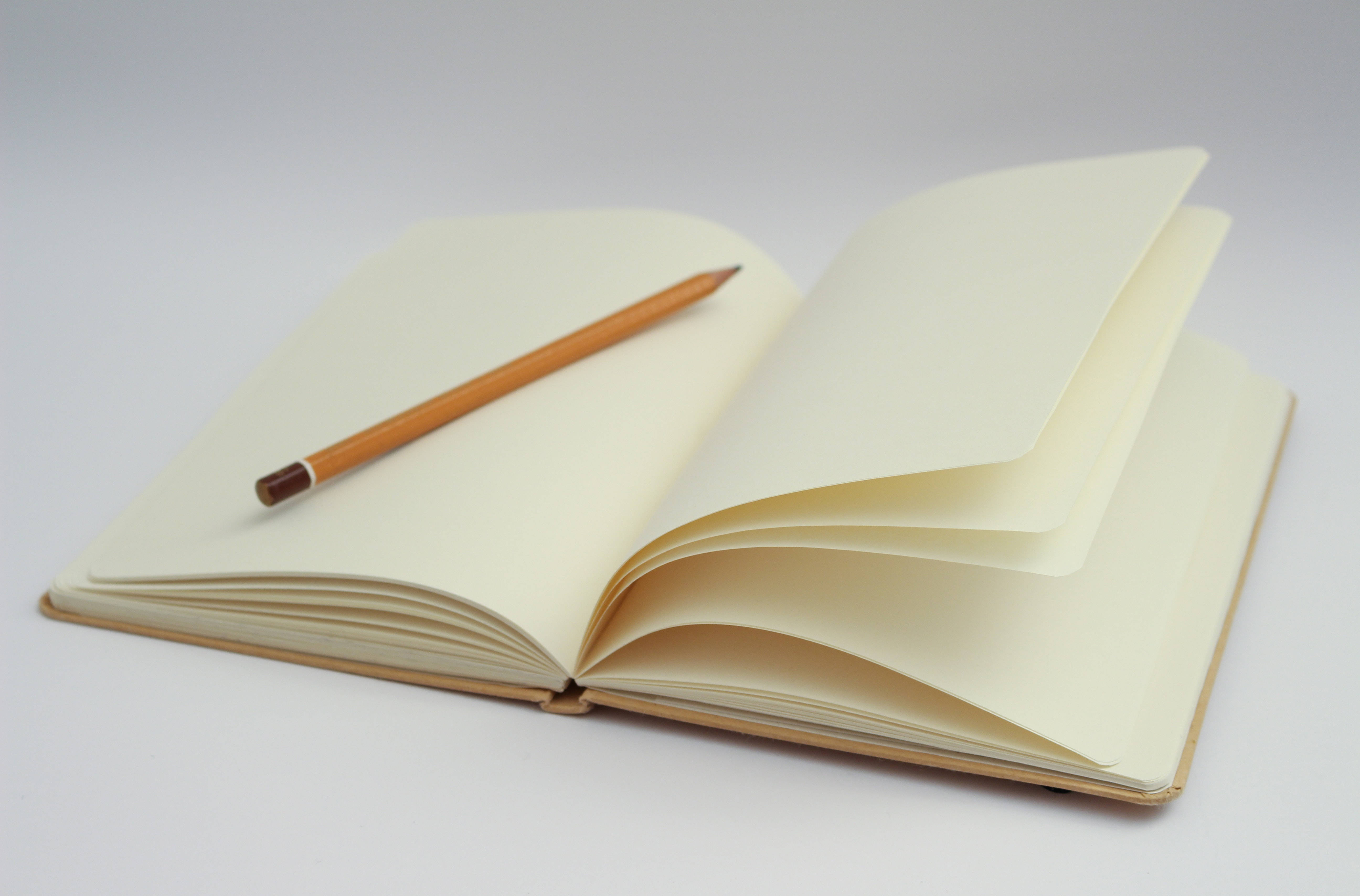 paper 桌布 壁紙 — 一本打開的奶油色筆記本，內頁空白，上面放著一支木鉛筆，背景為純白色。