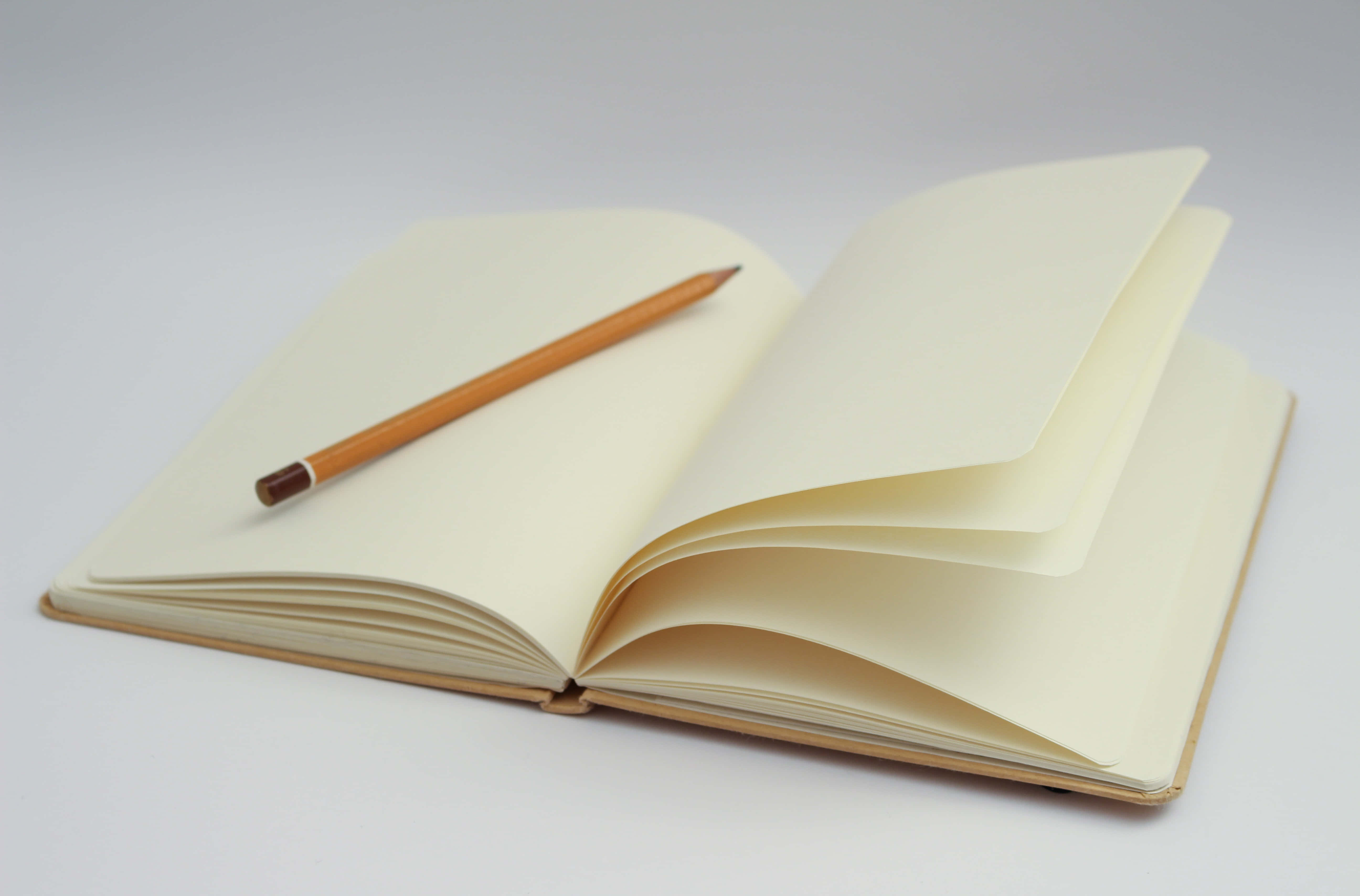 Diary 桌布 壁紙 — 一本打開的奶油色筆記本，內頁空白，還有一支木鉛筆，放在乾淨的白色表面上。