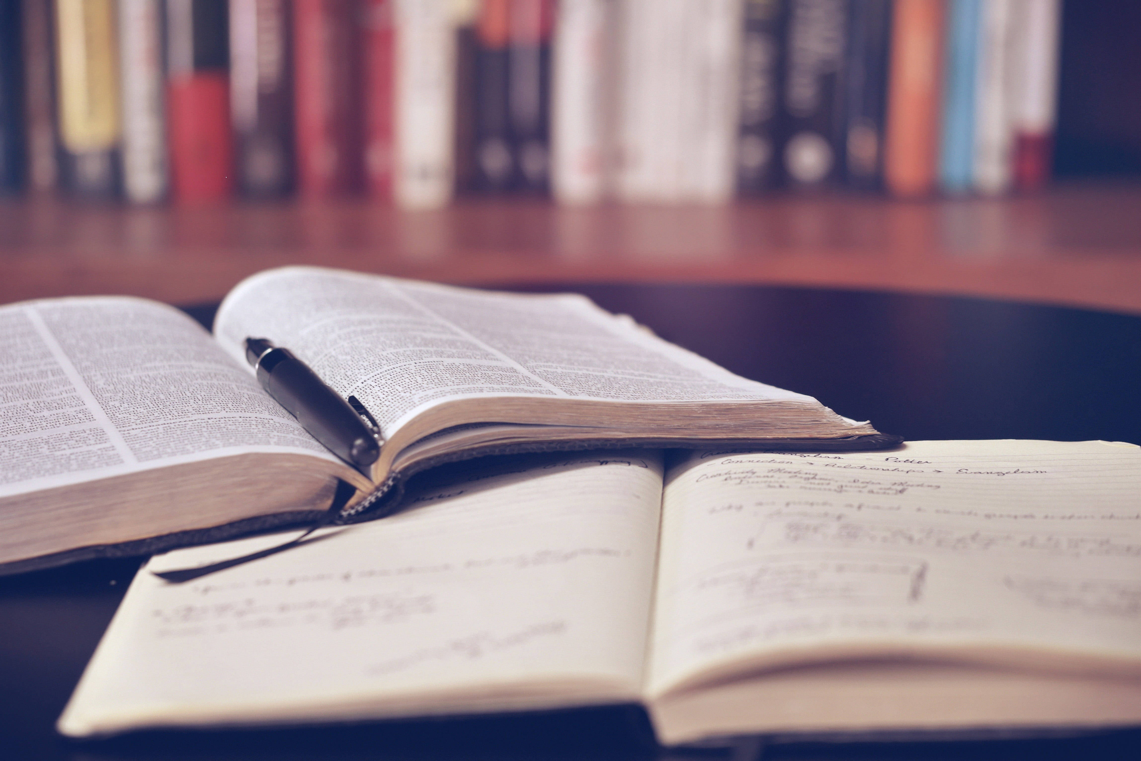 Reading 桌布 壁紙 — 一本打開的字典和筆記本，筆托放在暗色桌子上，背景是模糊的書架。