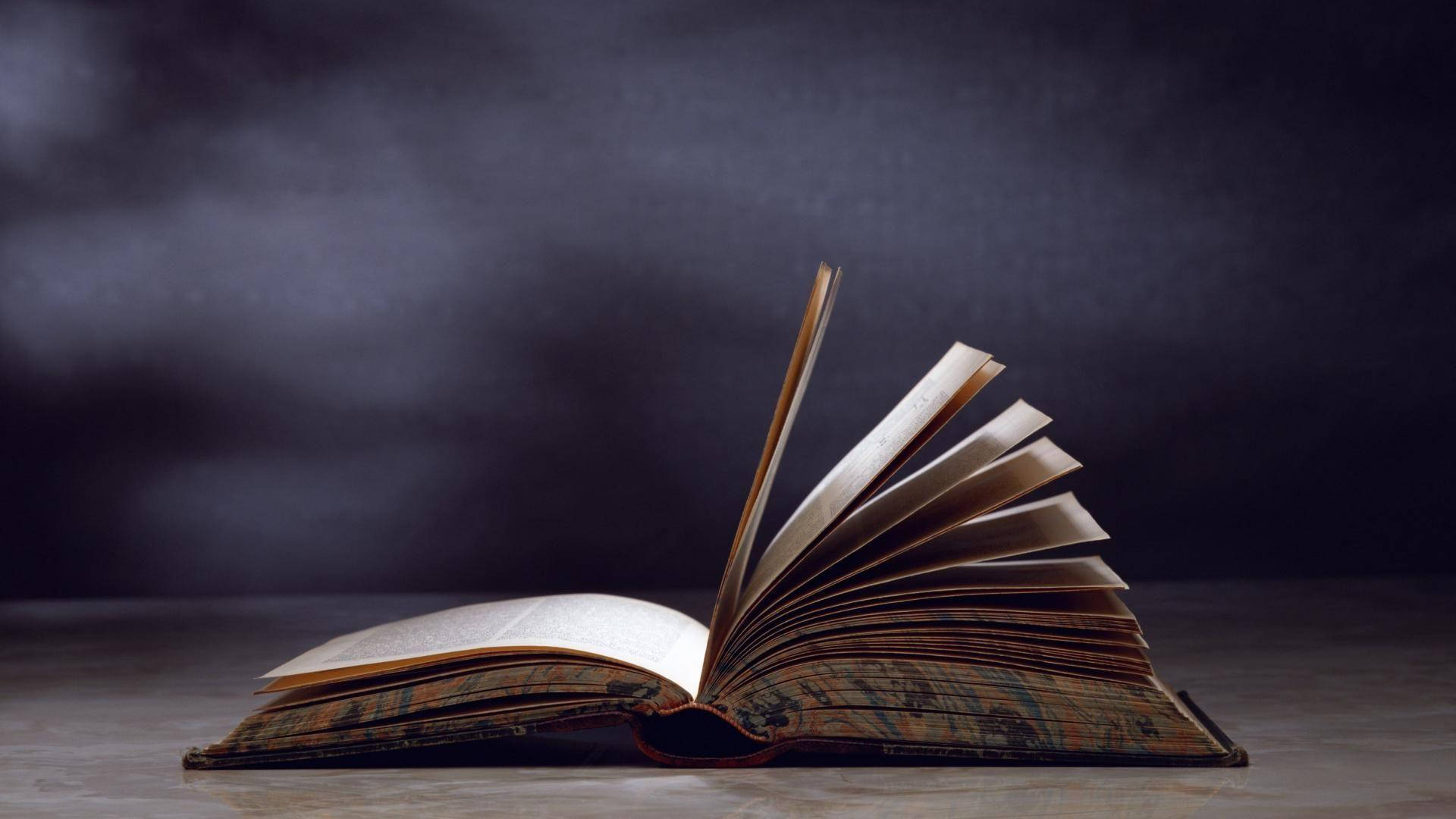 Educational 桌布 壁紙 — 一本打開的復古書，書頁呈扇形展開，放在木質表面上，背景陰暗而有氣氛。