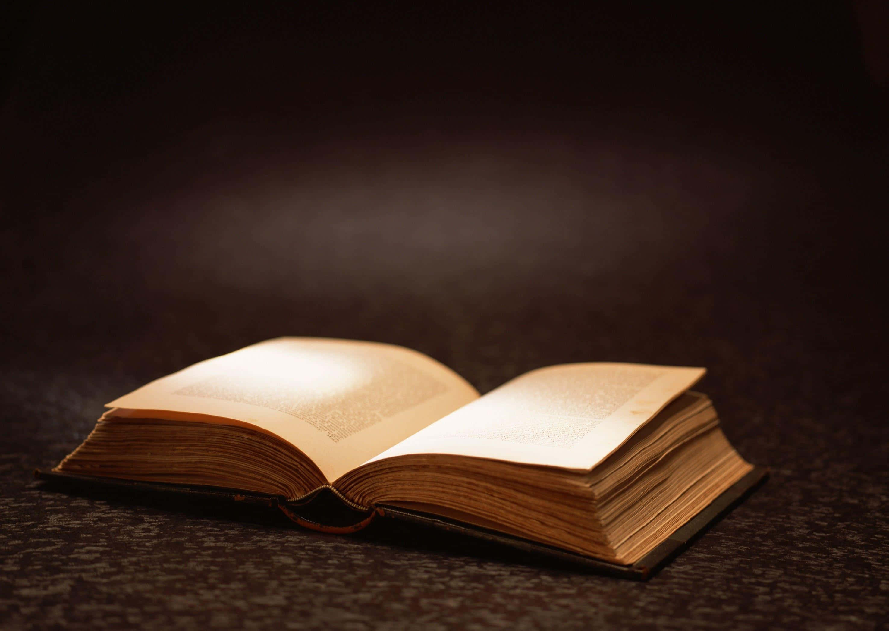 Learning 桌布 壁紙 — 一本打開的復古書在柔和光線下溫暖地發光，背景為深色紋理。