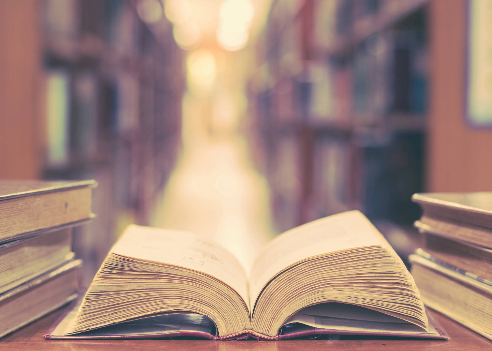 Dictionary 桌布 壁紙 — 一本打開的復古書本放在木桌上，位於燈光溫暖的圖書館走廊，兩旁是高聳的書架。