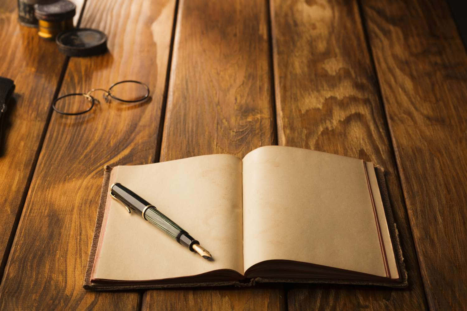 Diary 桌布 壁紙 — 一本打開的復古皮革筆記本和一支鋼筆放在溫暖的木桌上，旁邊有老花眼鏡和墨水瓶。