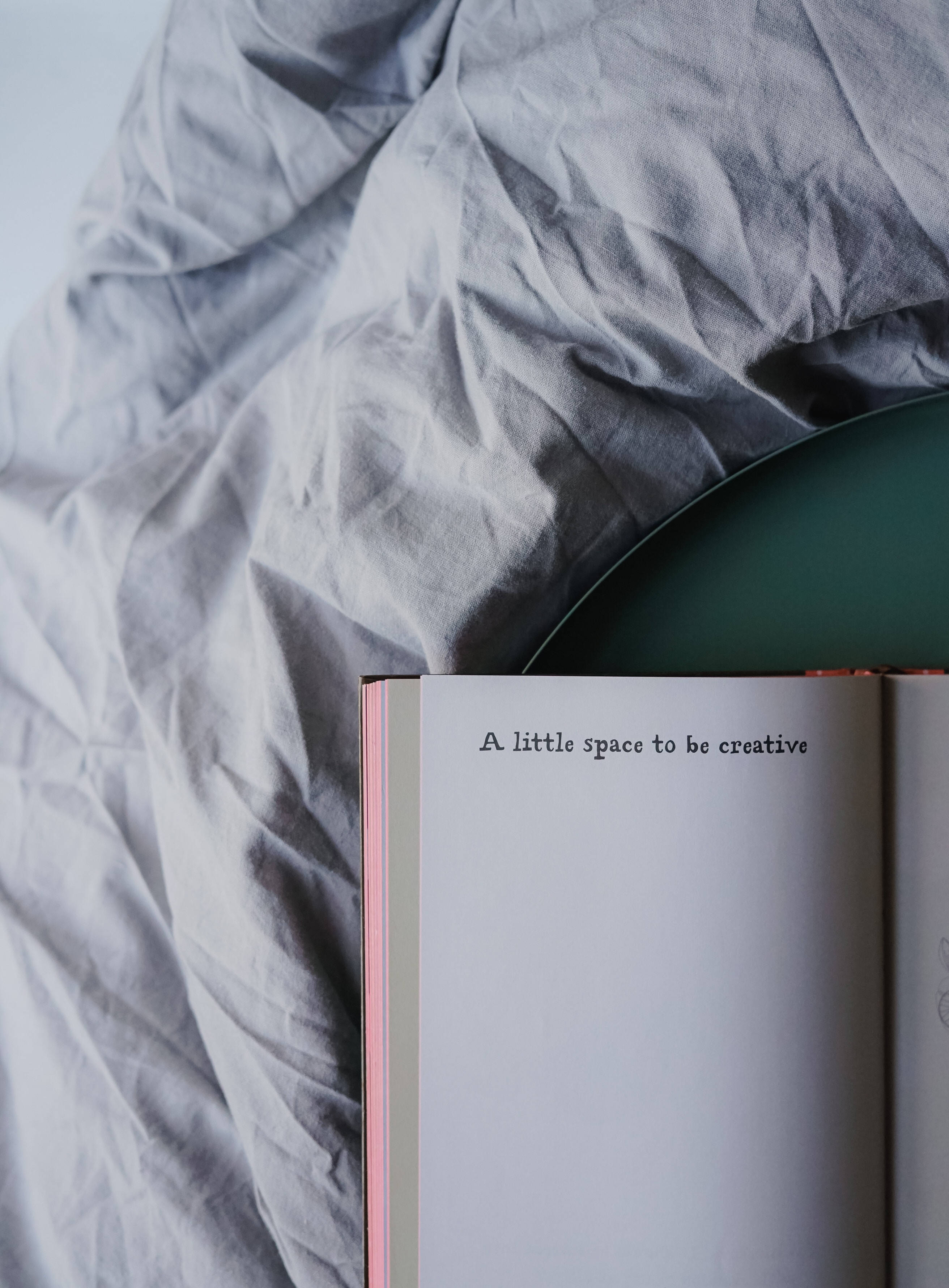 書本 桌布 壁紙 — 一本打開的書，上面寫著「A little space to be creative」，放在皺巴巴的灰色布料上，旁邊有一個青綠色碗。