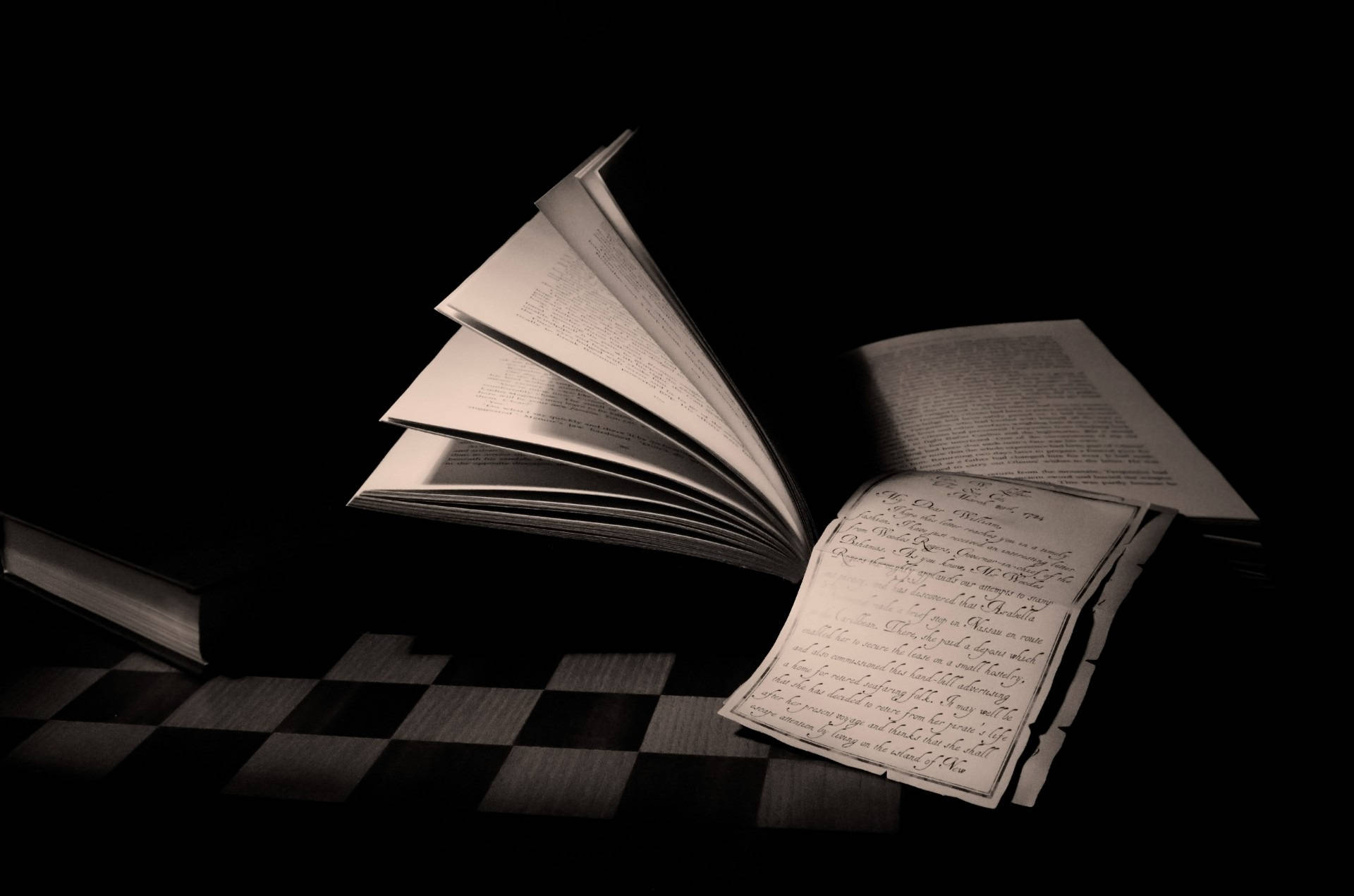 Reading 桌布 壁紙 — 一本打開的書，內有手寫頁面，放在格子表面上，黑色背景下的戲劇性聚光燈照射。