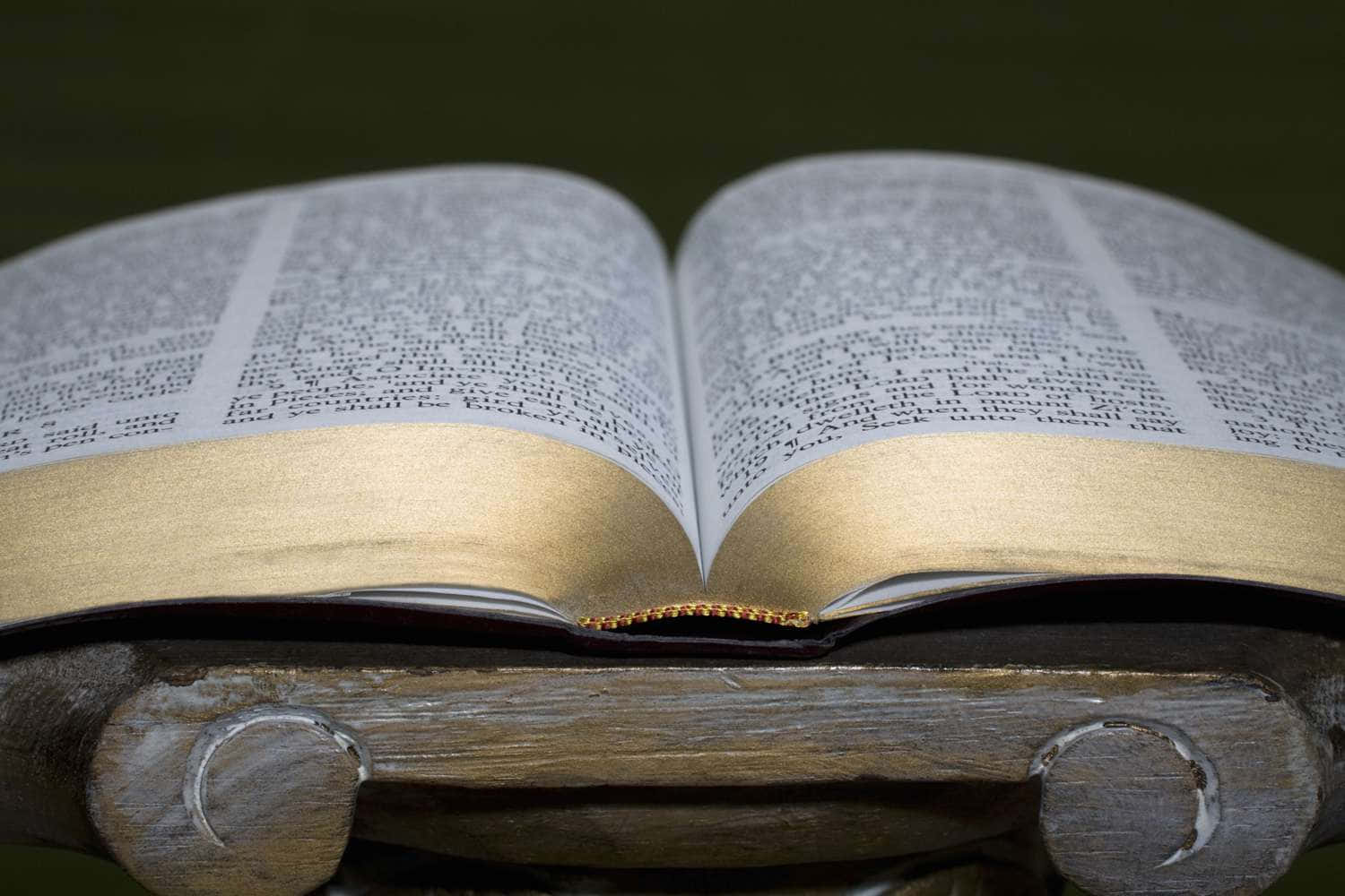 Scripture 桌布 壁紙 — 一本打開的書，帶有金色浮雕頁面，放在一個風化的木架上，背景是深綠色。