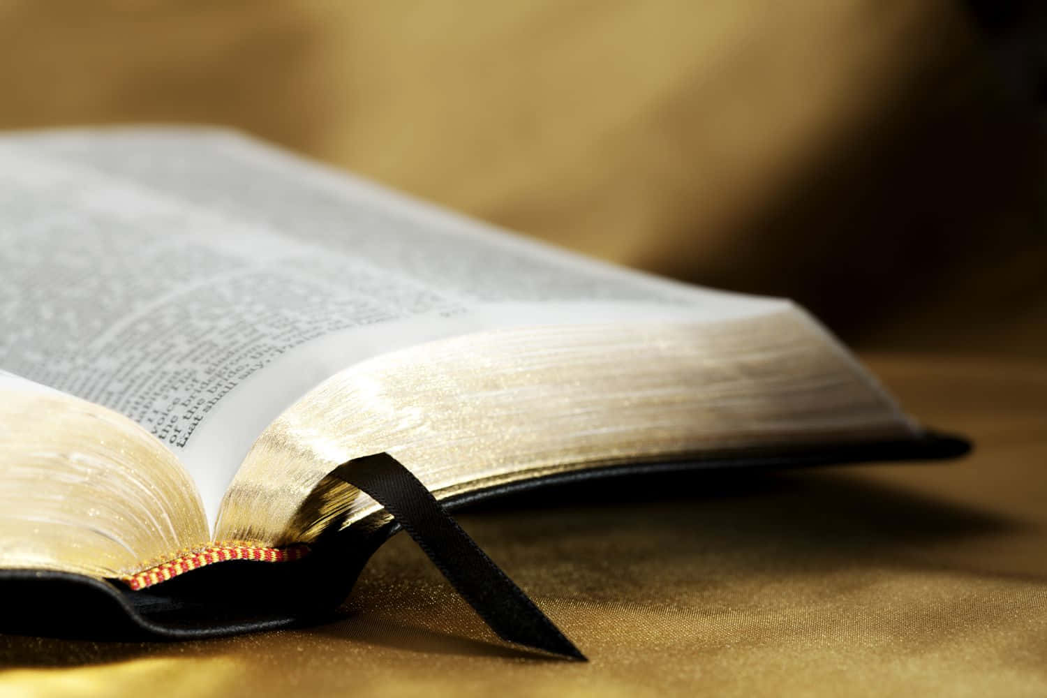 Biblical 桌布 壁紙 — 一本打開的書，帶有黑色絲帶書籤，放在金色紋理表面上，在溫暖的燈光下。