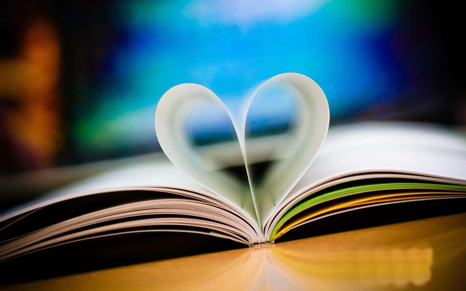 Heart 桌布 壁紙 — 一本打開的書，書頁摺成心形，放在木質表面上，背景是模糊的彩色。