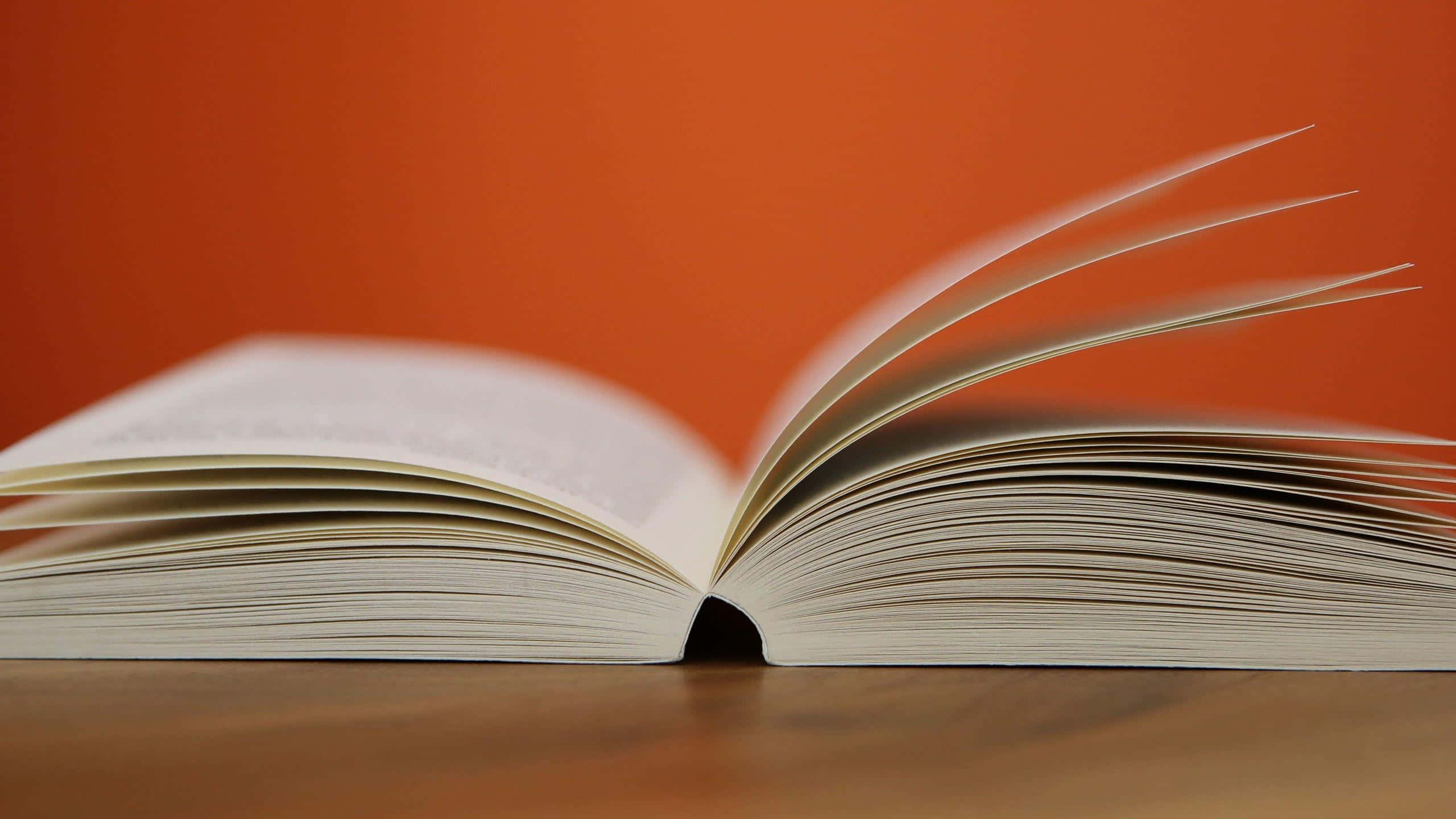 Learning 桌布 壁紙 — 一本打開的書，潔白的書頁放在木質表面上，背景是溫暖的橙色。