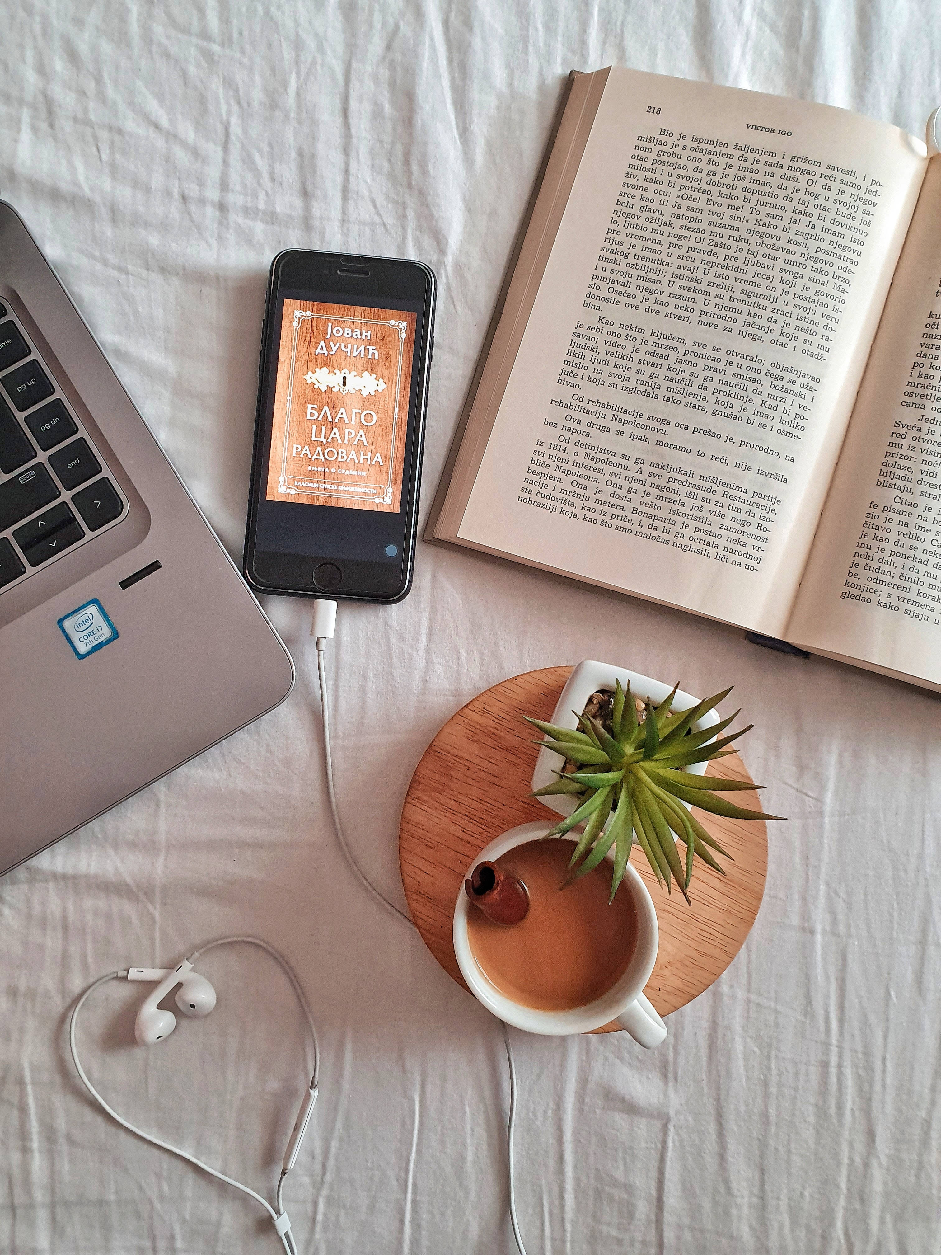Preppy Aesthetic 桌布 壁紙 — 一本打開的書、筆記型電腦、電話和咖啡杯整齊地擺放在白色床單上，營造舒適的閱讀時光。