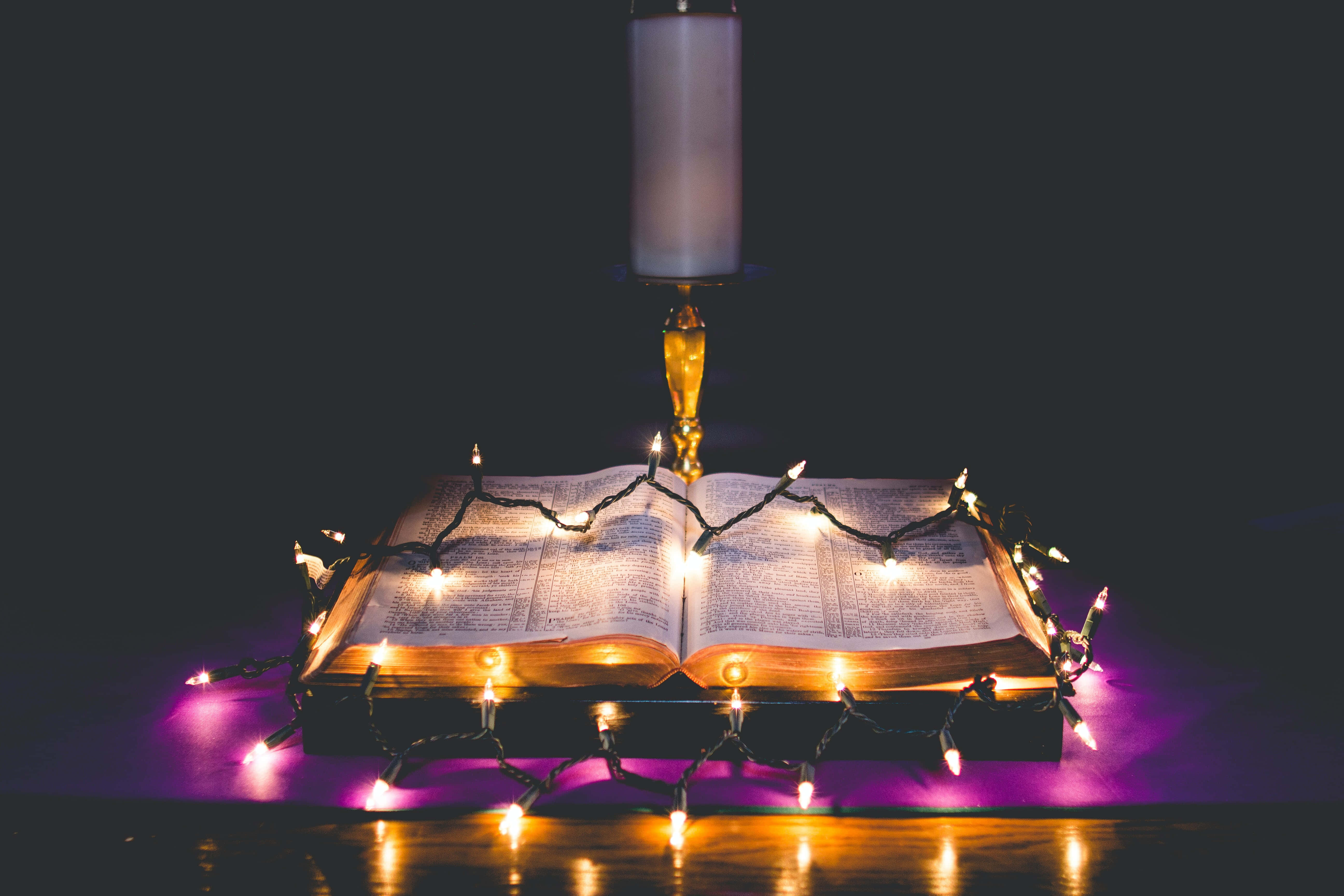 Christmas Light 桌布 壁紙 — 一本打開的書，被溫暖的串燈和高蠟燭照亮，背景是深紫色。
