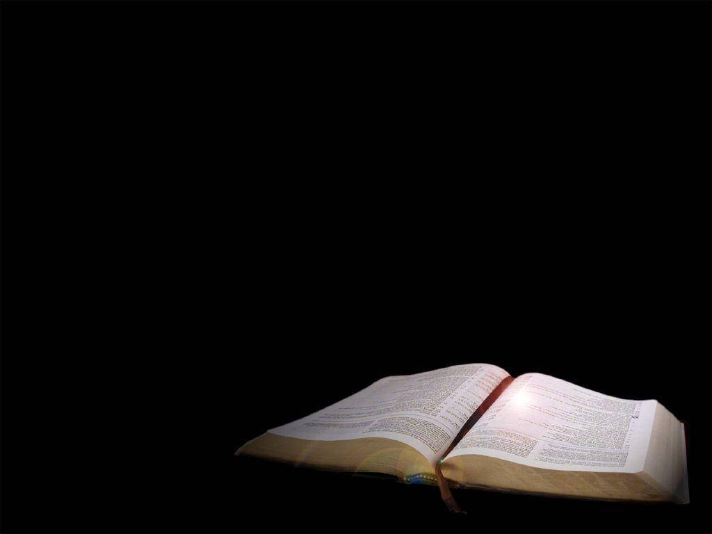 聖經 桌布 壁紙 — 一本打開的書在漆黑的背景下柔和地發光，將溫暖的光線投射在泛黃的書頁上。