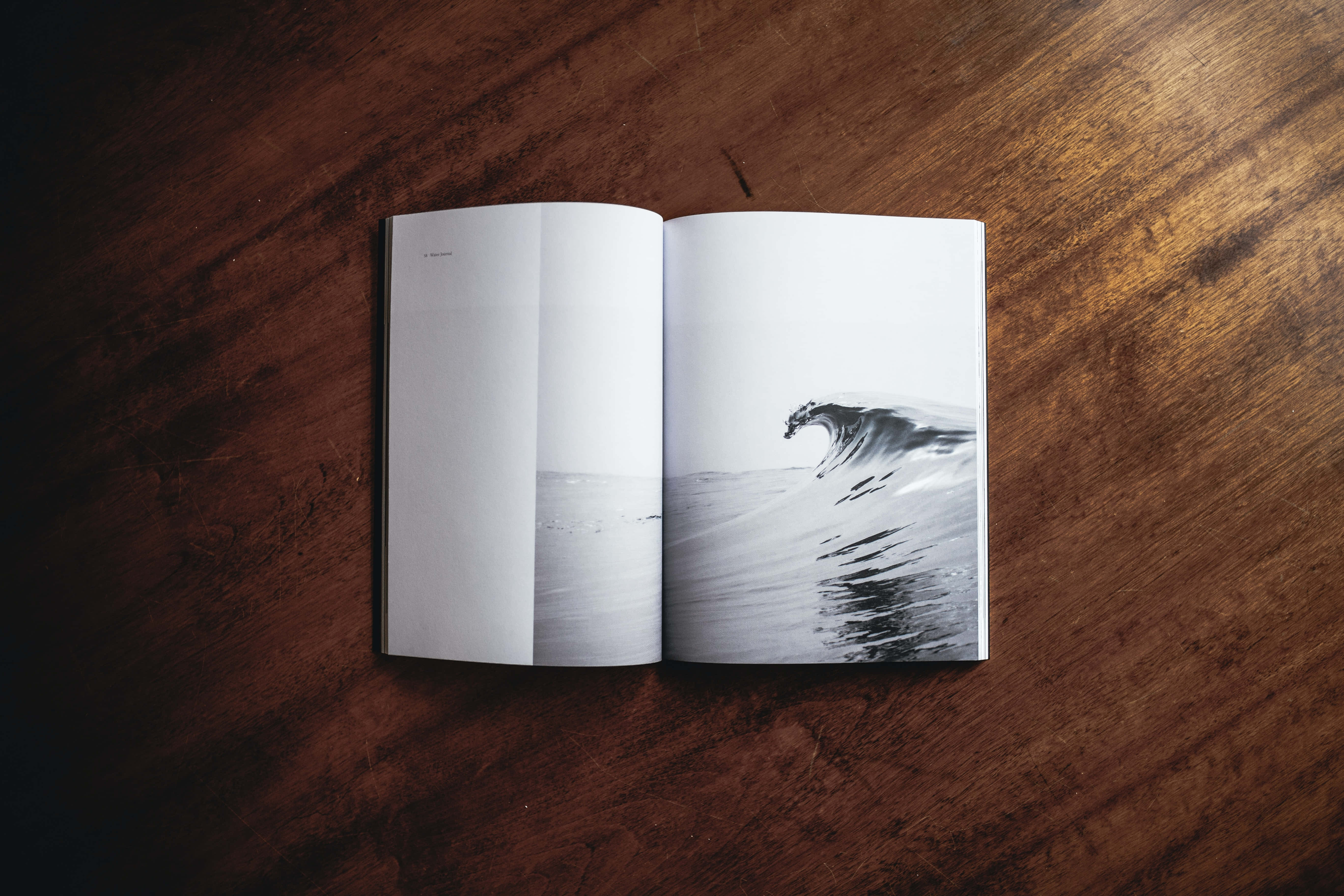 Magazine 桌布 壁紙 — 一本打開的書放在木桌上，展示了一張捲曲海浪的戲劇性黑白照片。
