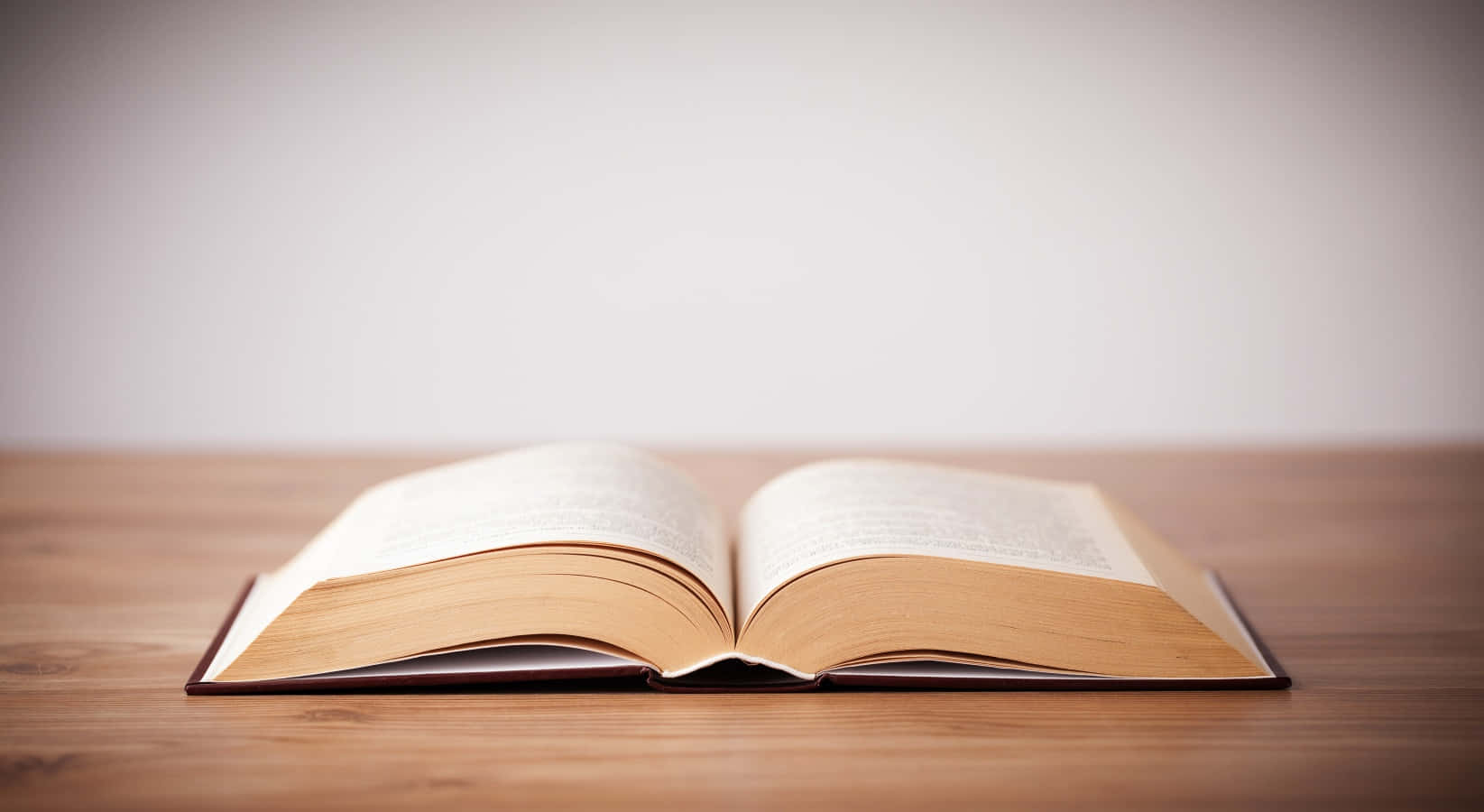 Open Book 桌布 壁紙 — 一本打開的書放在木質表面上，光線柔和，景深較淺。