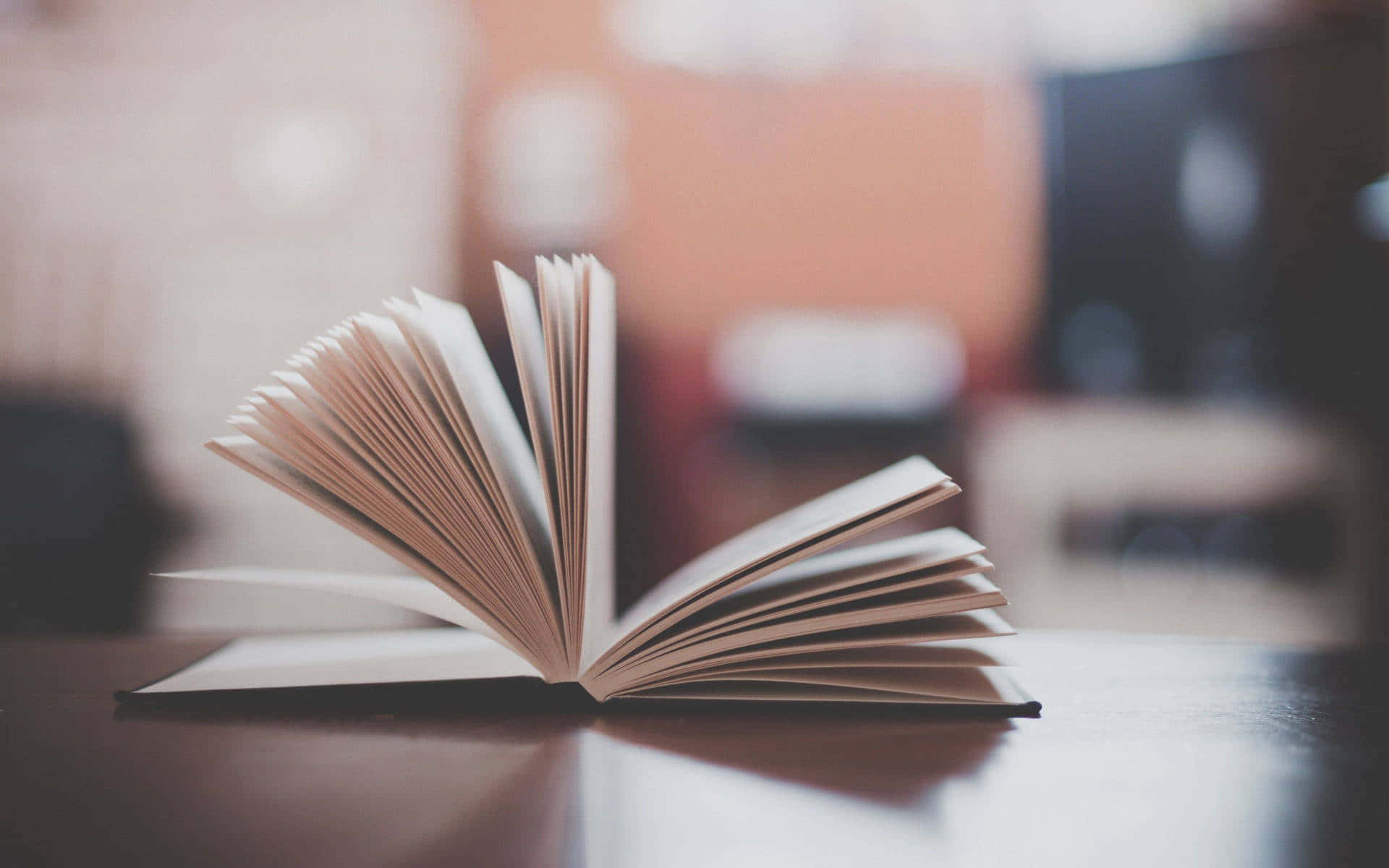 Open Book 桌布 壁紙 — 一本打開的書放在木質表面上，帶有柔和溫暖的燈光和模糊的背景家具。