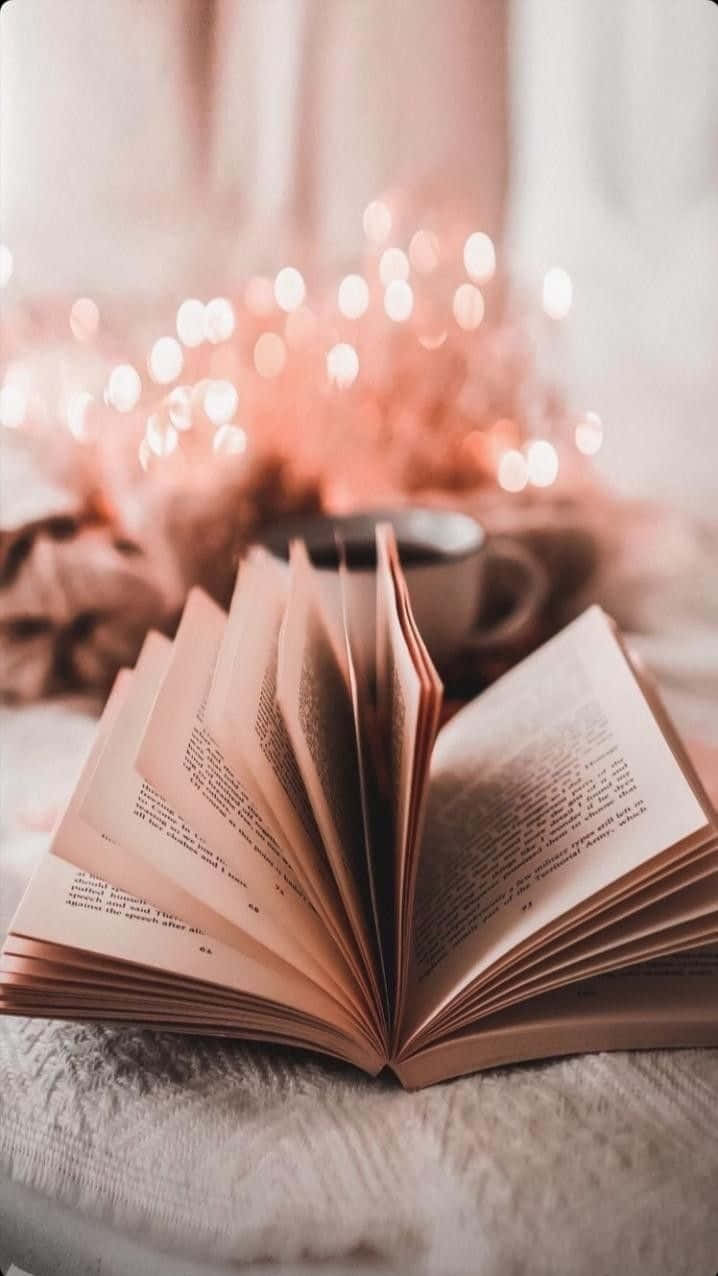 Aesthetic Books 桌布 壁紙 — 一本打開的書放在柔軟的毯子上，背景中溫暖的仙女燈柔和地閃爍。