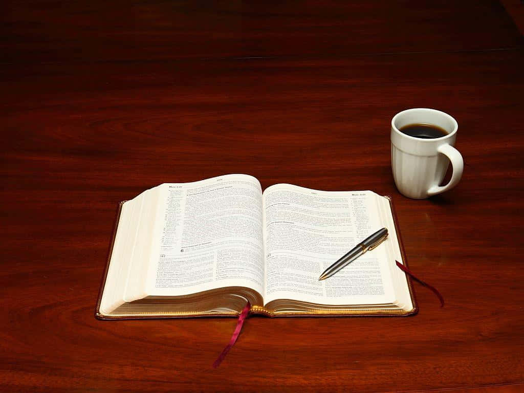 Bible Study 桌布 壁紙 — 一本打開的書本連同一支筆放在一杯咖啡旁邊，置於一張質感豐富的木桌上，營造出寧靜的書房氛圍。