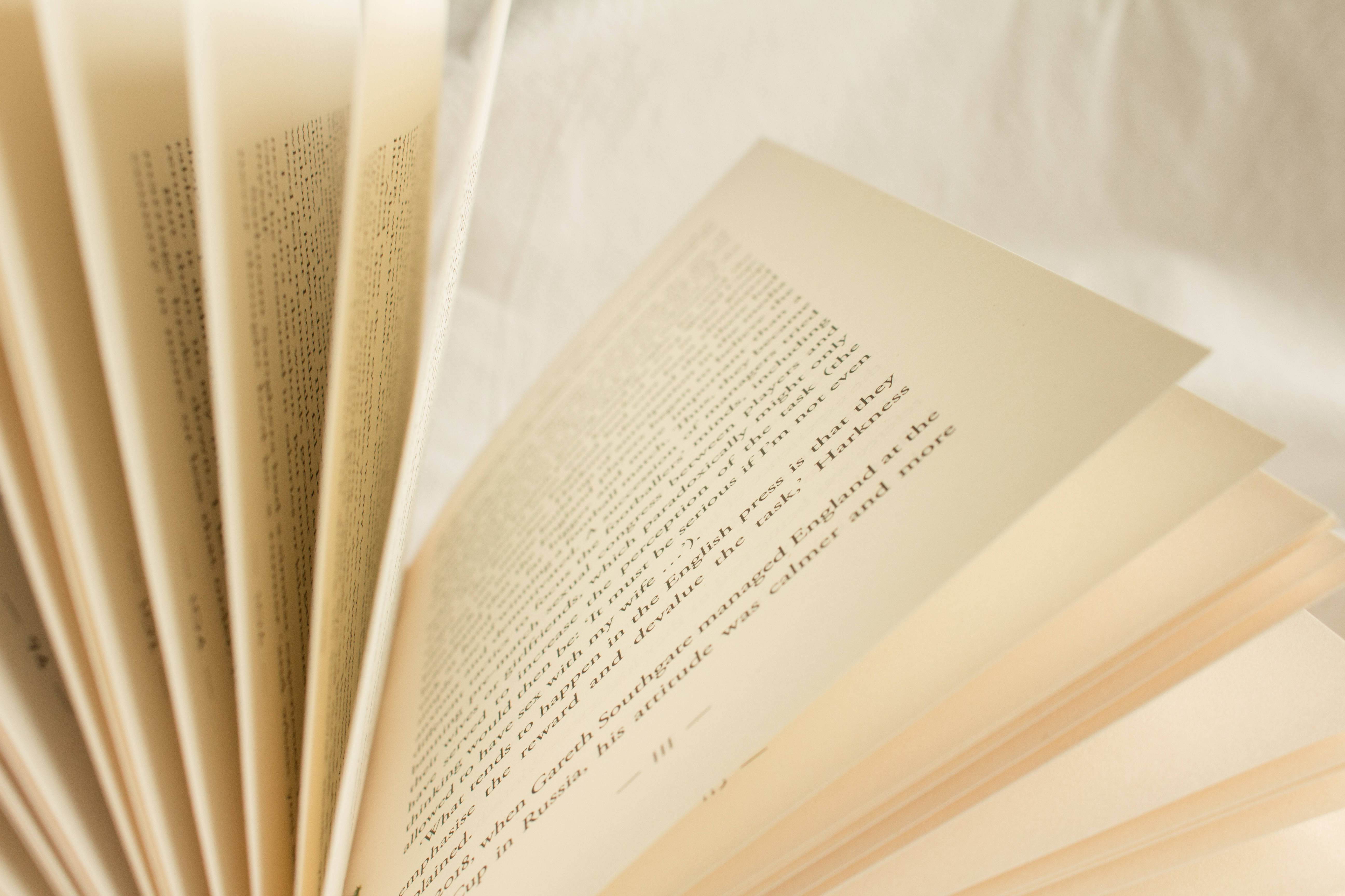 米色風格 桌布 壁紙 — 一本打開的書的特寫，奶油色頁面和黑色文字，在白色布料背景上被自然光柔和地照亮。