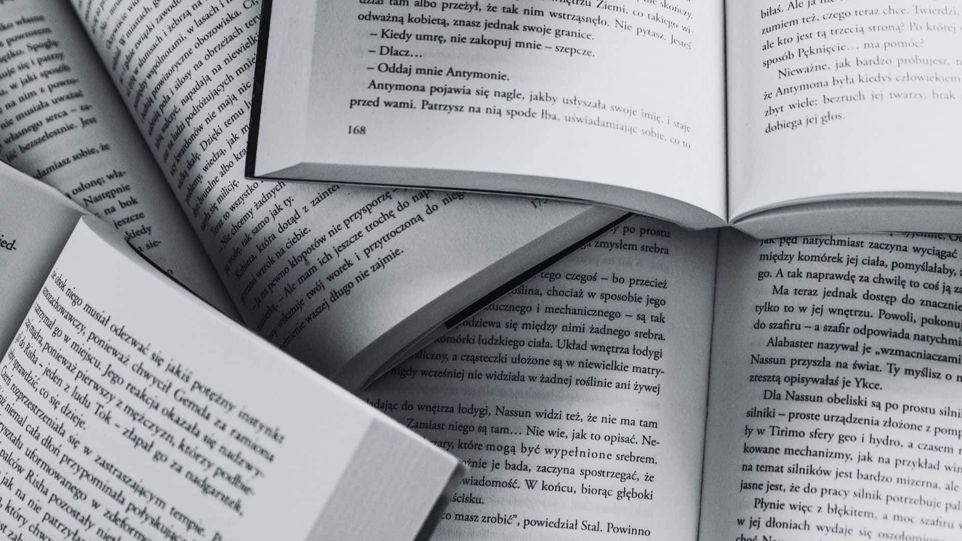 Black And White Book 桌布 壁紙 — 一本打開的書的特寫，帶有波蘭語文字，顯示第168頁和散落的頁面，處於柔焦狀態。