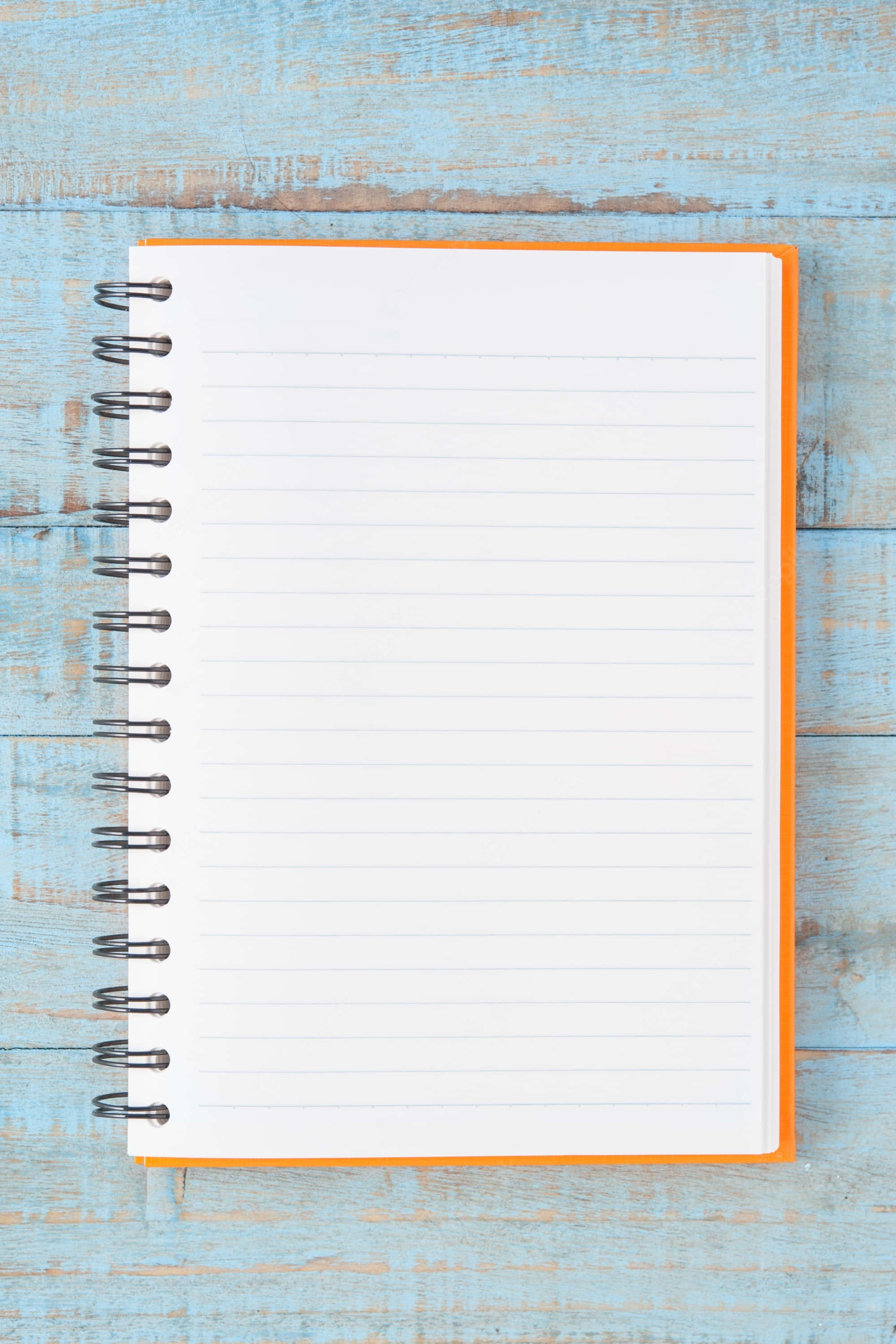 Notebook 桌布 壁紙 — 一本打開的橙色螺旋筆記本，內有空白橫線頁面，放在經風化的藍色木質表面上。