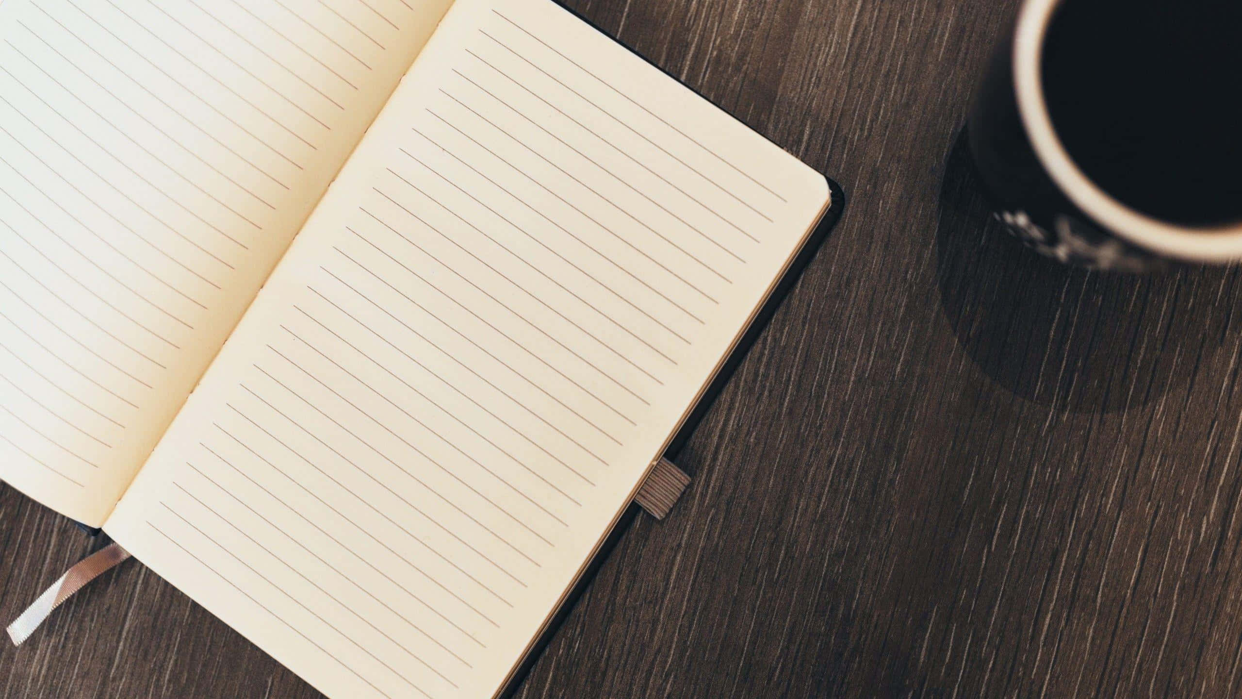 Notebook 桌布 壁紙 — 一本打開的橫線筆記本放在一個深色咖啡杯旁邊，置於一張華麗的木桌上，俯視圖。