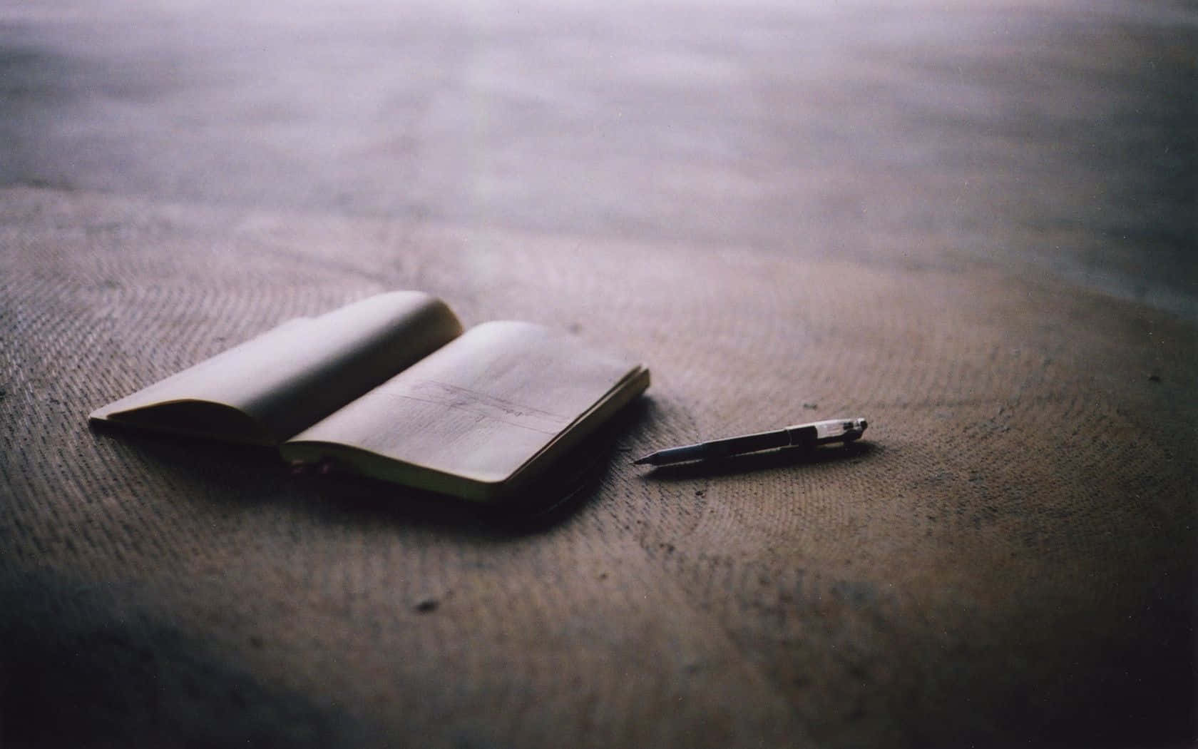 Notebook 桌布 壁紙 — 一本打開的筆記本和一支筆放在有紋理的木質表面上，環境光線柔和。