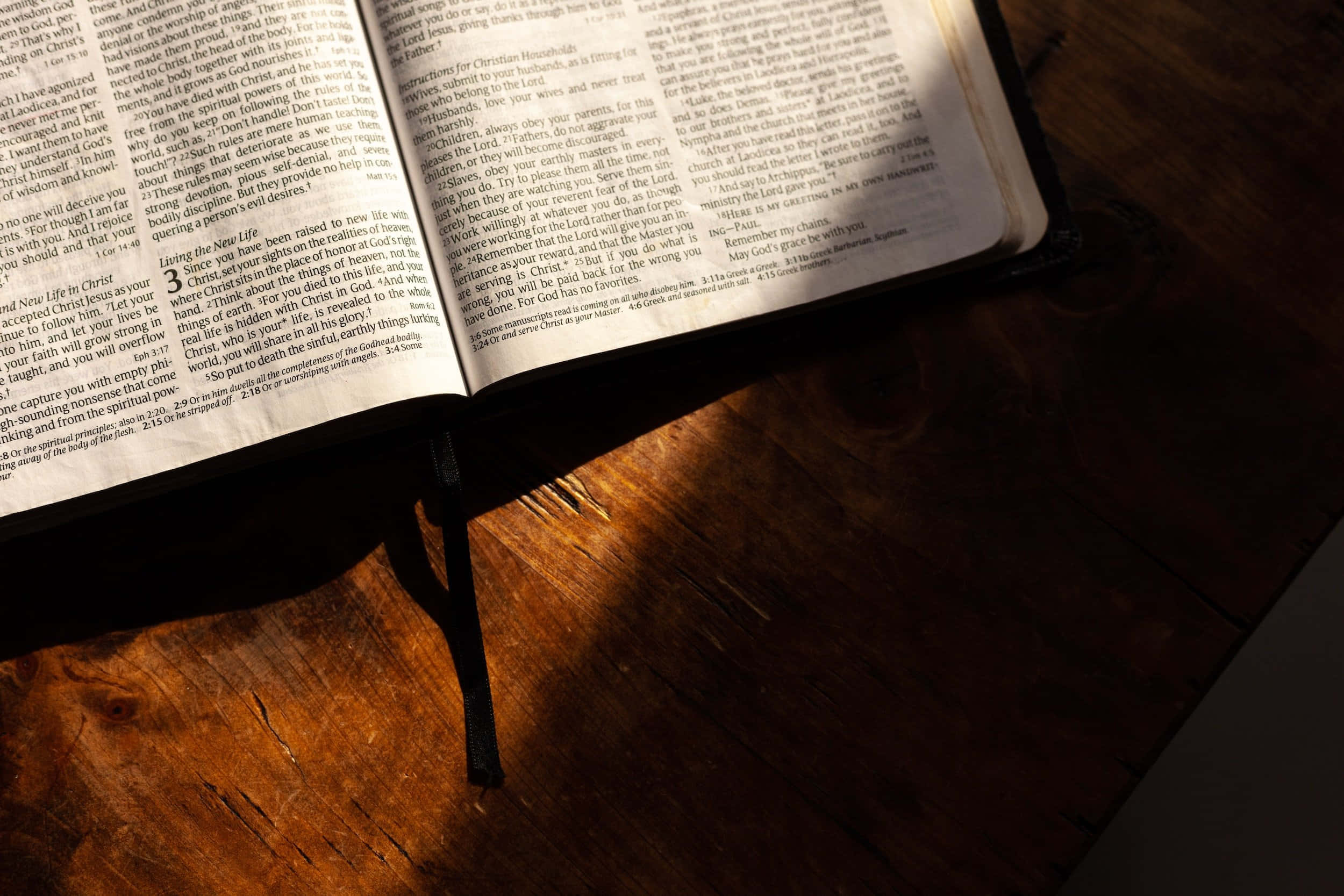Scripture 桌布 壁紙 — 一本打開的聖經放在木桌上，沐浴在溫暖的金色光芒中，在書頁上投下柔和的陰影。