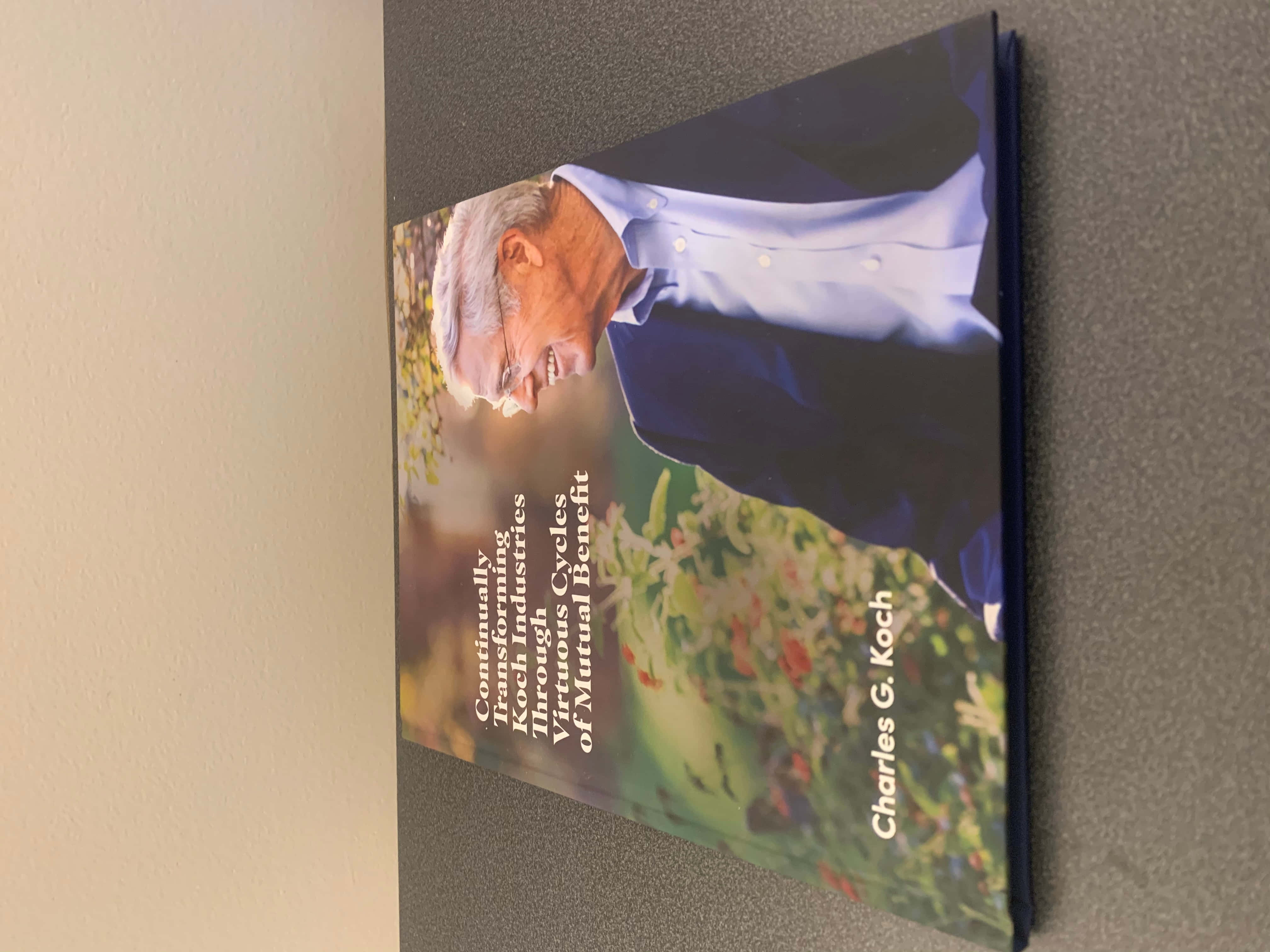 書本 桌布 壁紙 — 一本由Charles G. Koch撰寫的書《Continually Improving Koch Industries Through Virtuous Cycles of Mutual Benefit》斜放在灰色表面上。