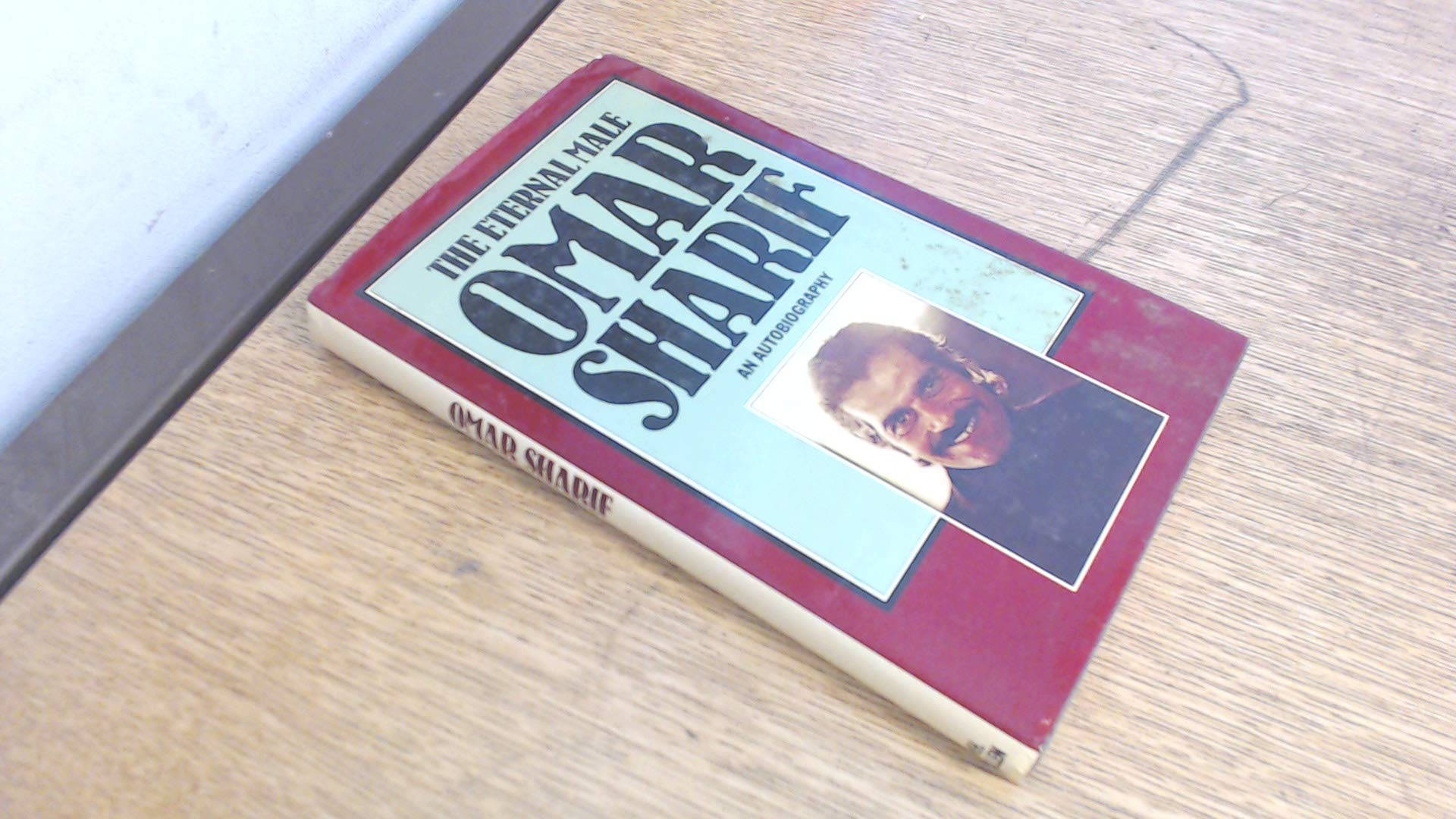 書本 桌布 壁紙 — 一本破舊的紅色書本，書名為「The Eternal Tale Omar Sharif」，傾斜地放在淺色木質表面上。