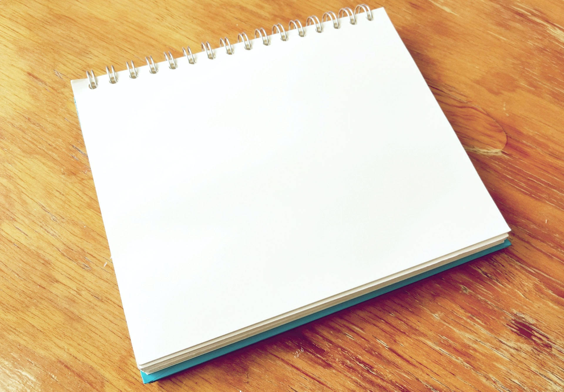 paper 桌布 壁紙 — 一本空白螺旋筆記本放在溫暖的木桌上，木紋清晰可見，光線自然。