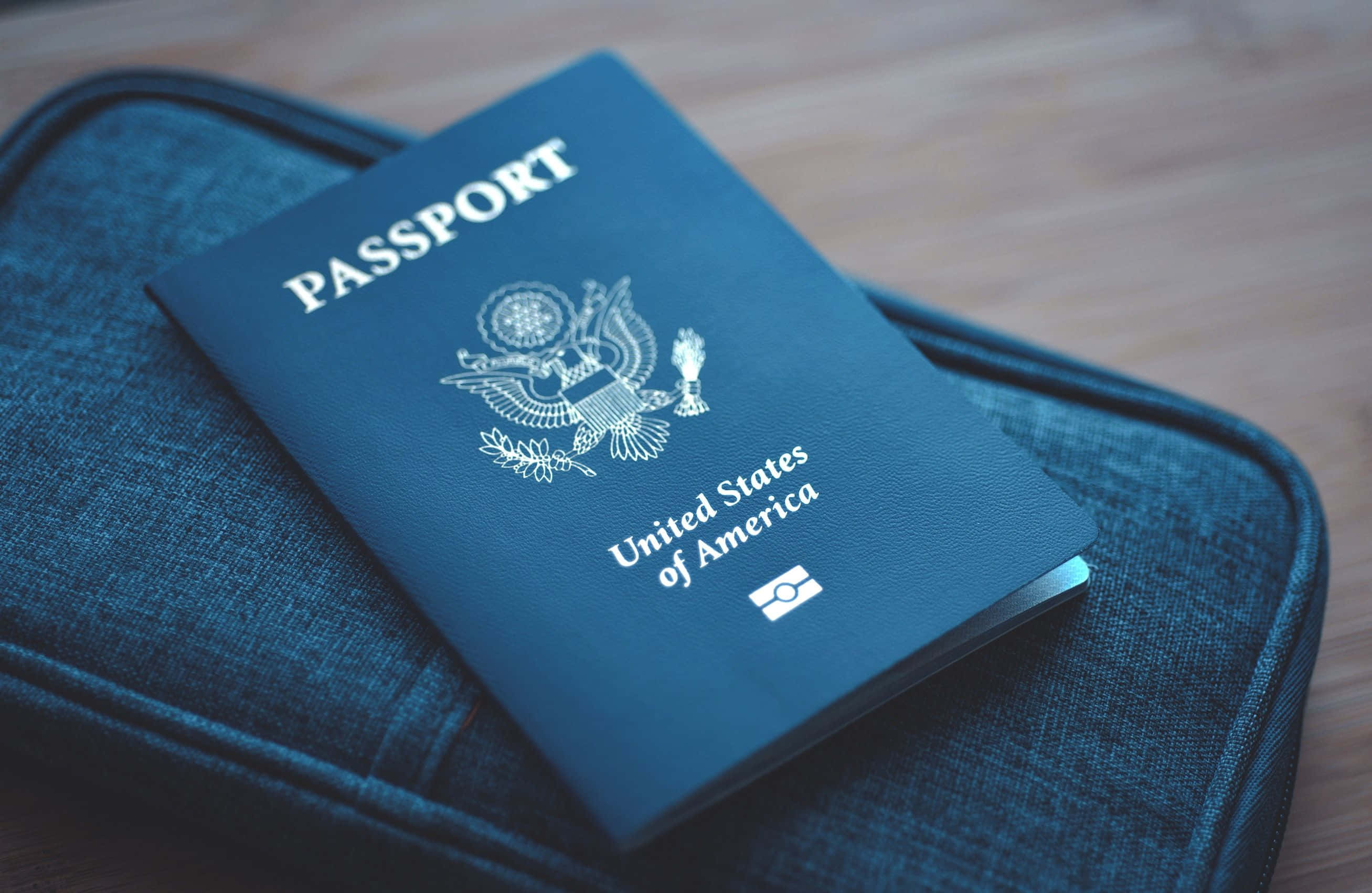 Passport 桌布 壁紙 — 一本美國護照放在木質表面上的一個藍色紋理保護套上，柔和自然光照射。