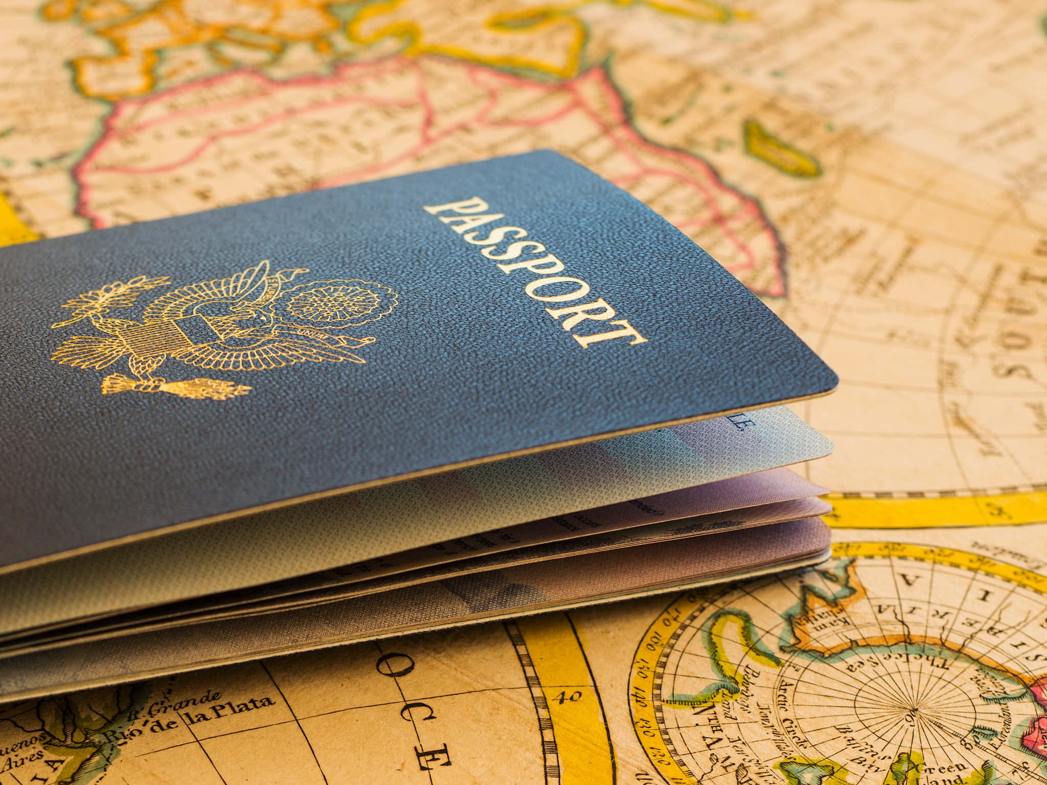 Passport 桌布 壁紙 — 一本藍色護照帶有金色壓花，放在復古世界地圖頁面上，展現旅行夢想。