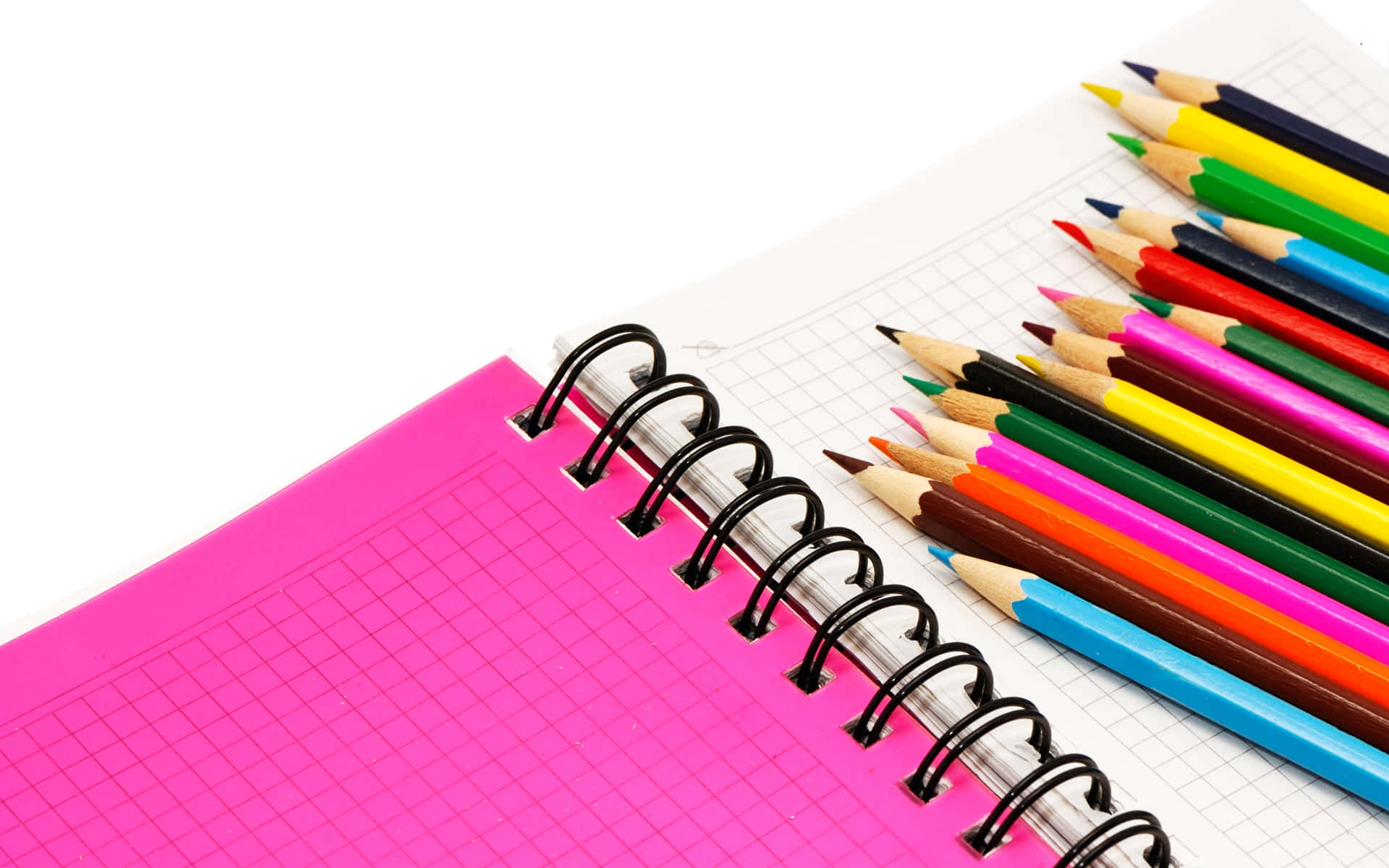 pencil 桌布 壁紙 — 一本鮮粉紅色螺旋筆記本，內有方格紙，旁邊整齊排列著色彩繽紛的削尖顏色鉛筆，置於潔白表面上。