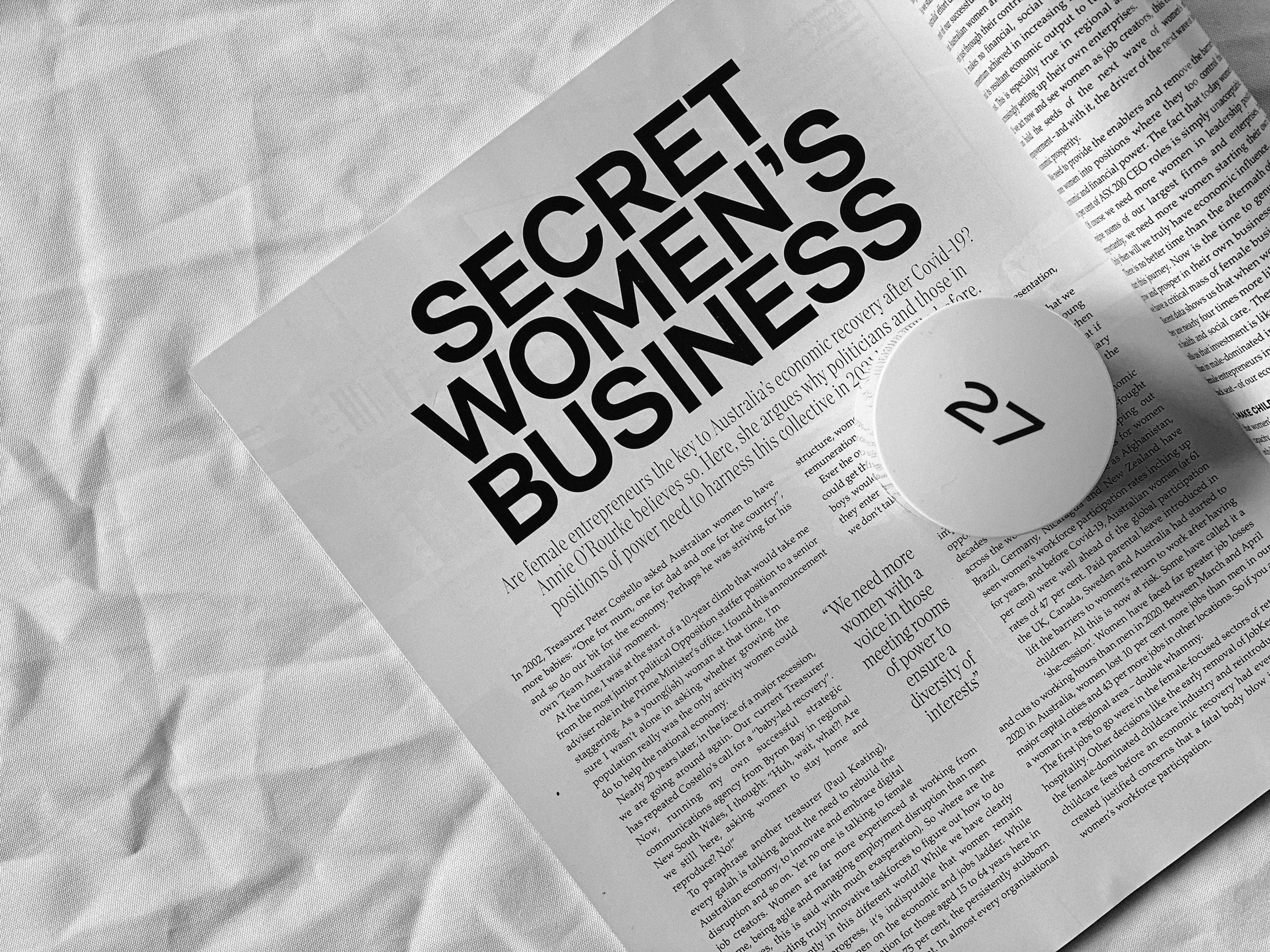 Magazine 桌布 壁紙 — 一本黑白雜誌跨頁，標題為 Secret Women's Business，放在皺巴巴的白色布料表面上，有一個圓形頁碼標記顯示數字 27。