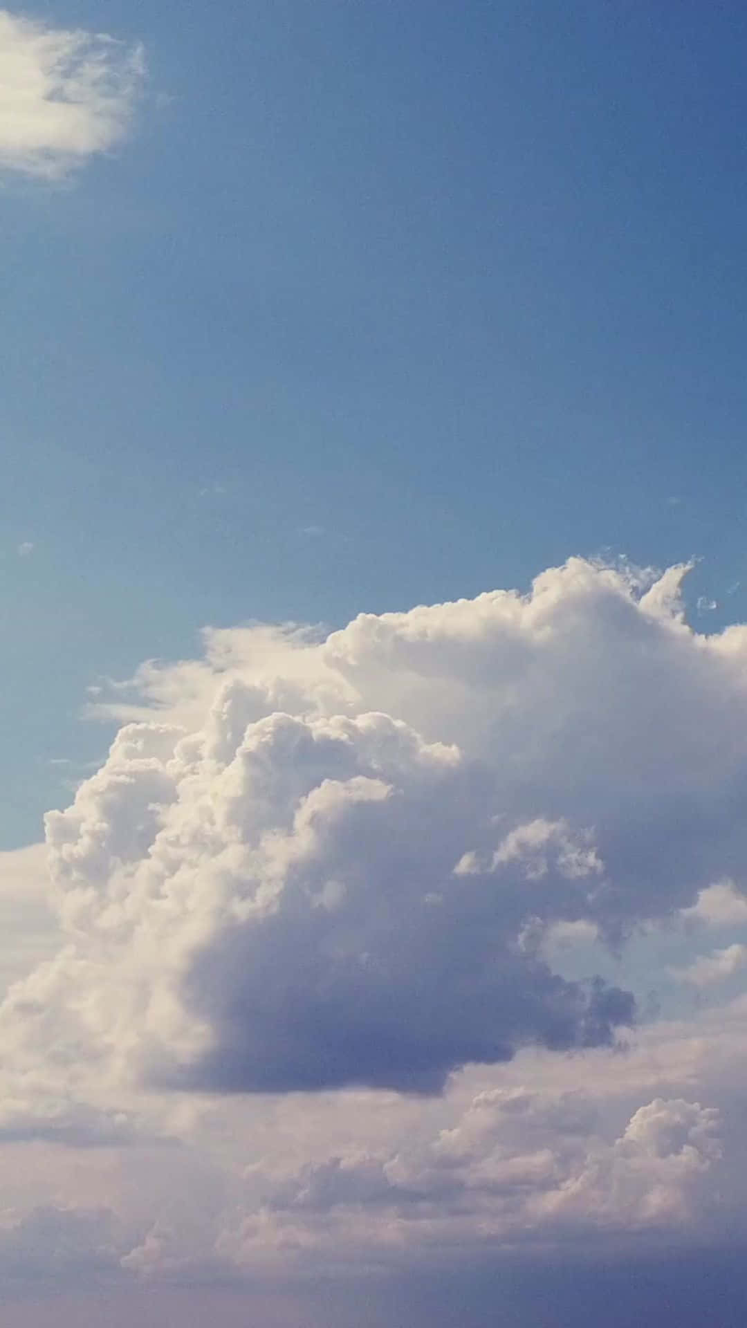 雲朵 桌布 壁紙 — 一朵巨大蓬鬆的白雲主宰著清澈的藍天，地平線附近帶有柔和的粉彩色調。