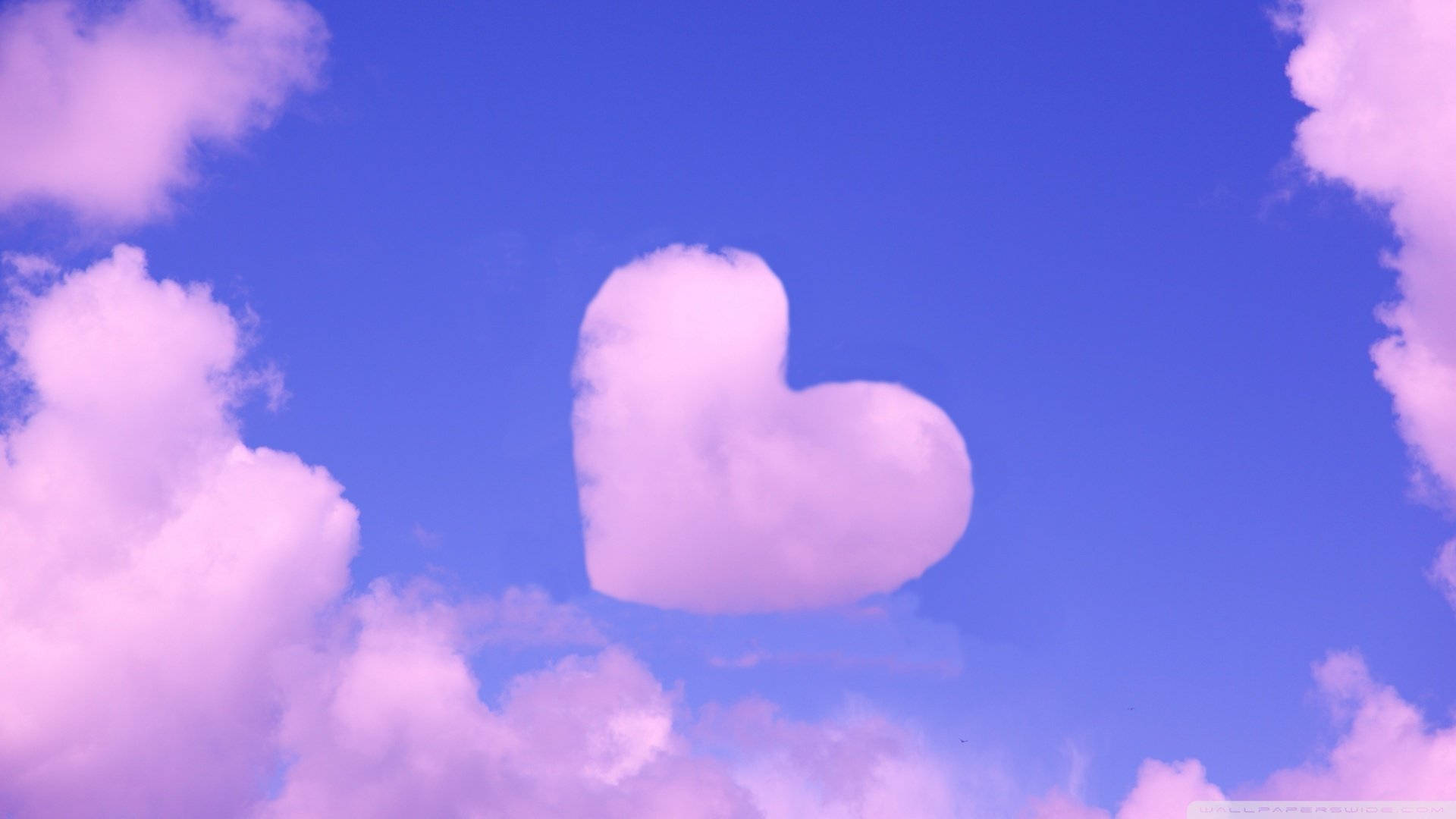 Cute Pink Cloud 桌布 壁紙 — 一朵柔軟的粉紅色心形雲朵寧靜地漂浮在由蓬鬆粉彩雲朵框住的鮮豔藍天中。